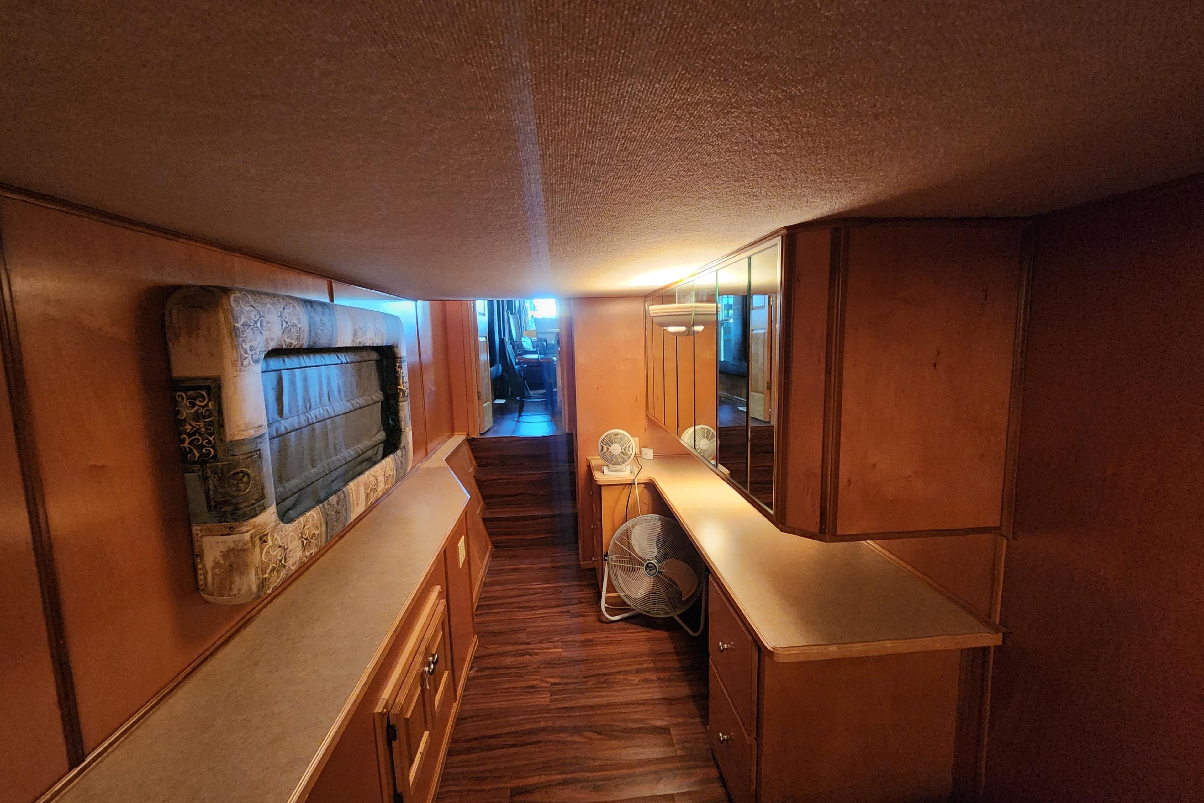 Narrow wooden interior of a 2000 Sharpe 85 houseboat with cabinets and a fan.