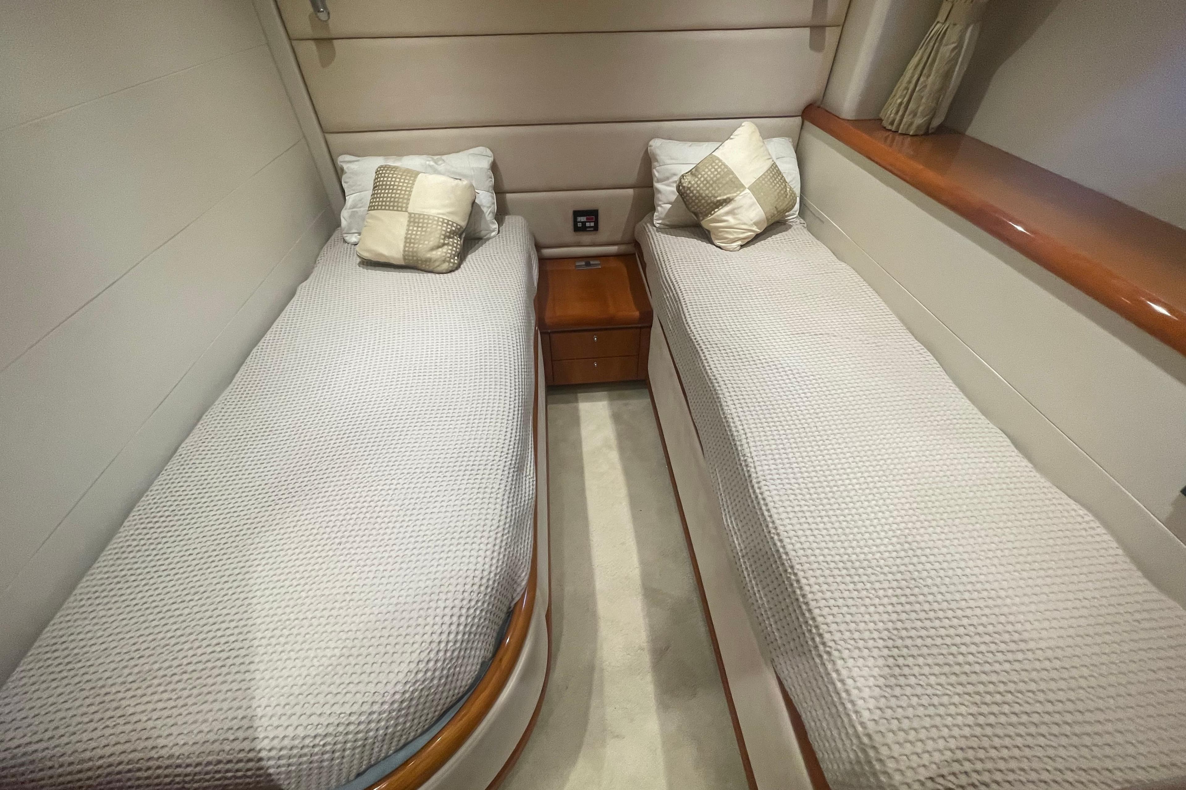 Twin beds in a 2003 Sunseeker Predator 68 yacht cabin, featuring elegant bedding and cushions.