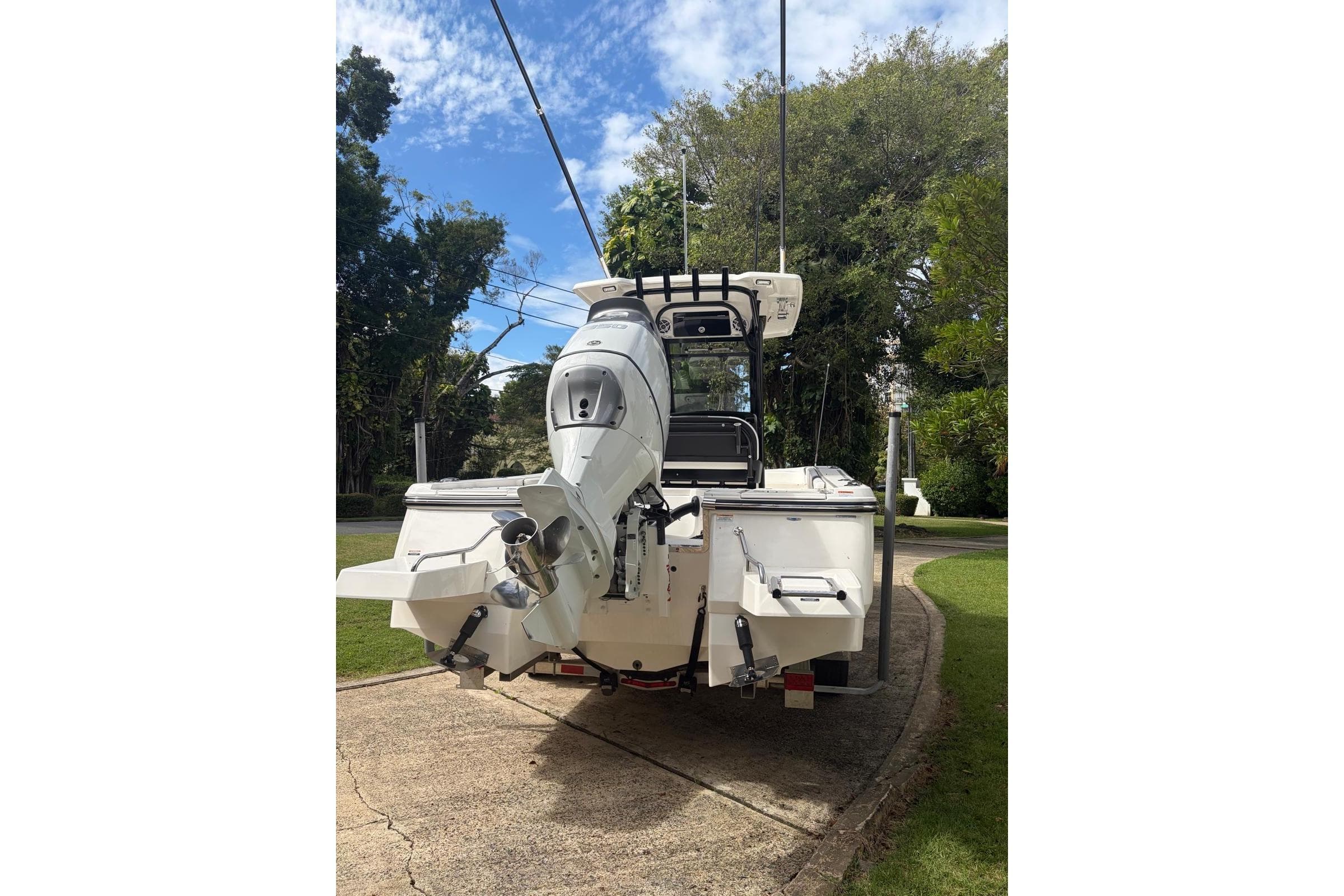 2023 Robalo 266 Cayman boat, rear view, parked on a driveway with lush greenery.