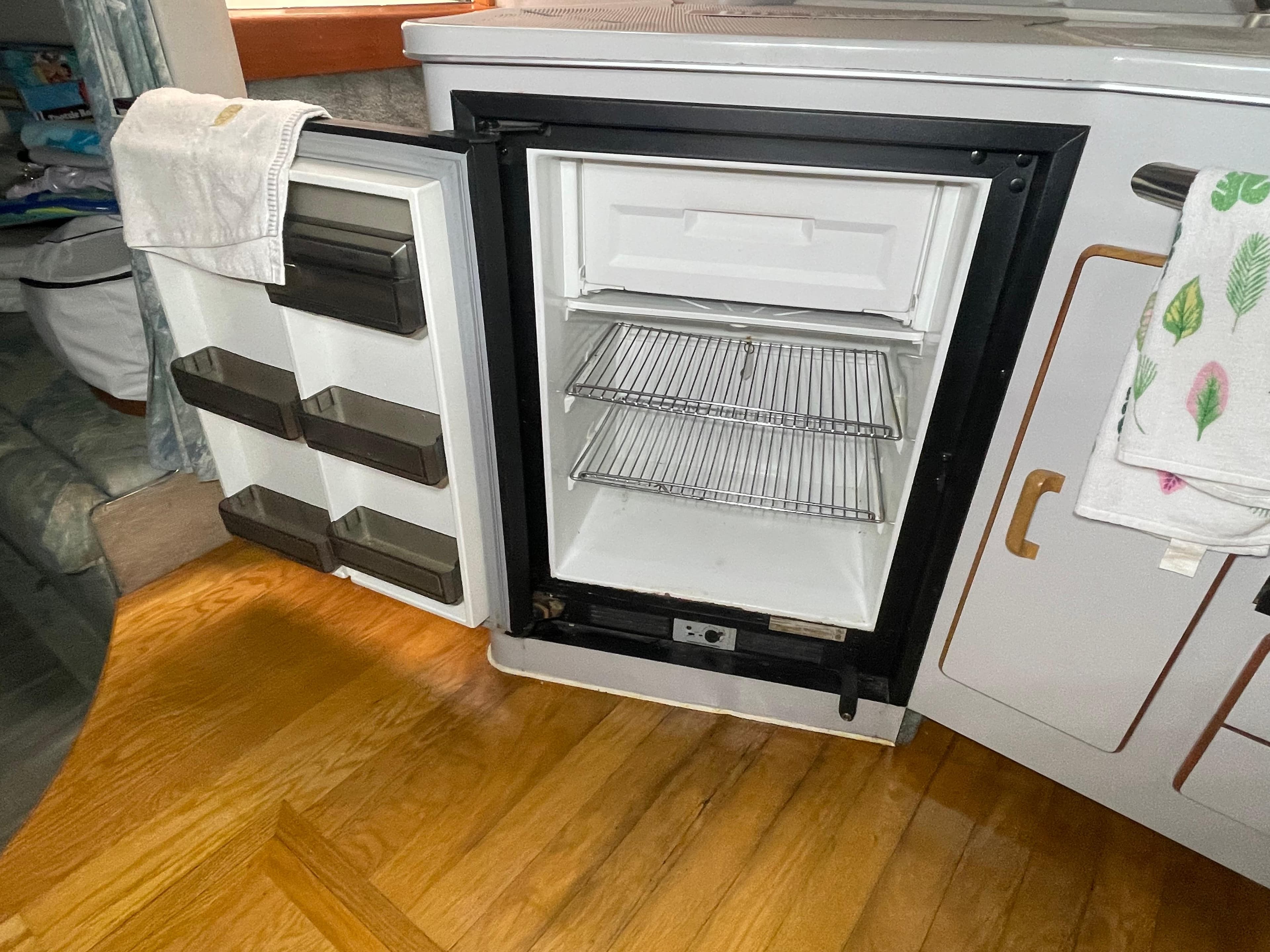 Open refrigerator inside 1991 Sea Ray 350 Sundancer boat, featuring wooden flooring and storage shelves.