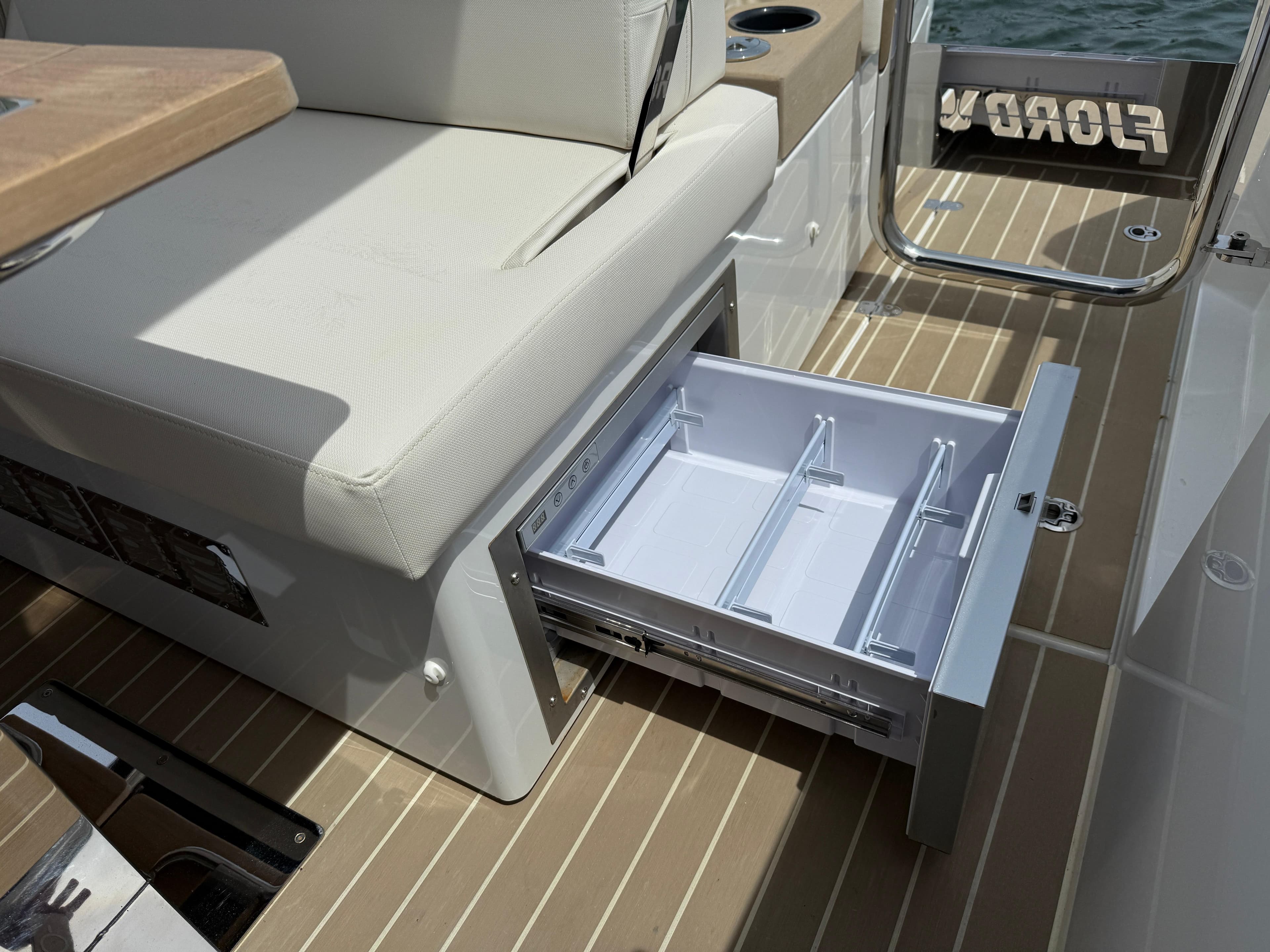Open storage drawer on 2025 Fjord 39 XP boat, featuring beige seating and wood-patterned flooring.