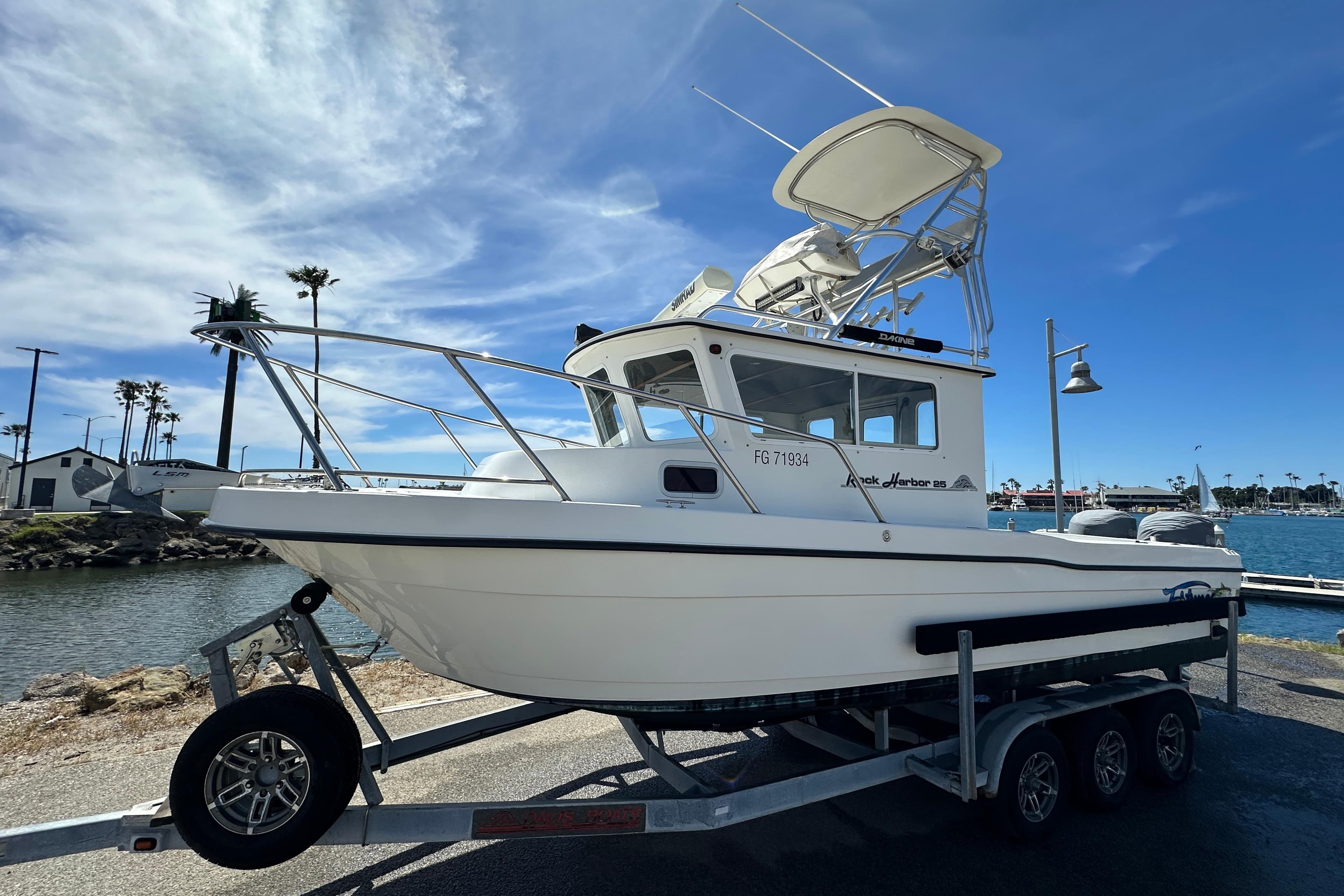 2012 Davis Rock Harbor 25 boat on trailer by waterfront, under clear blue sky.