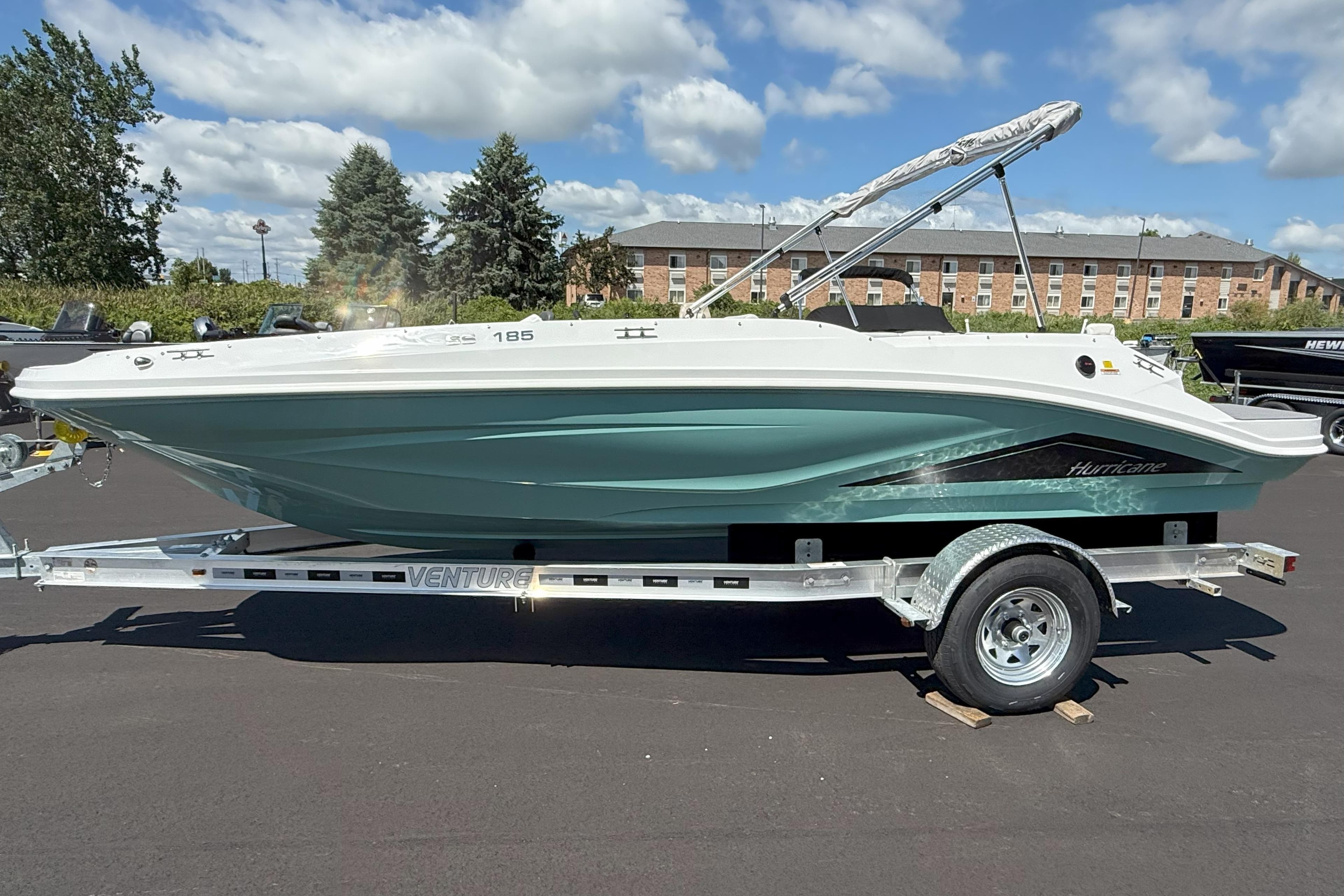 2026 Hurricane SunDeck Sport 185 OB boat on trailer, parked outdoors under a cloudy sky.