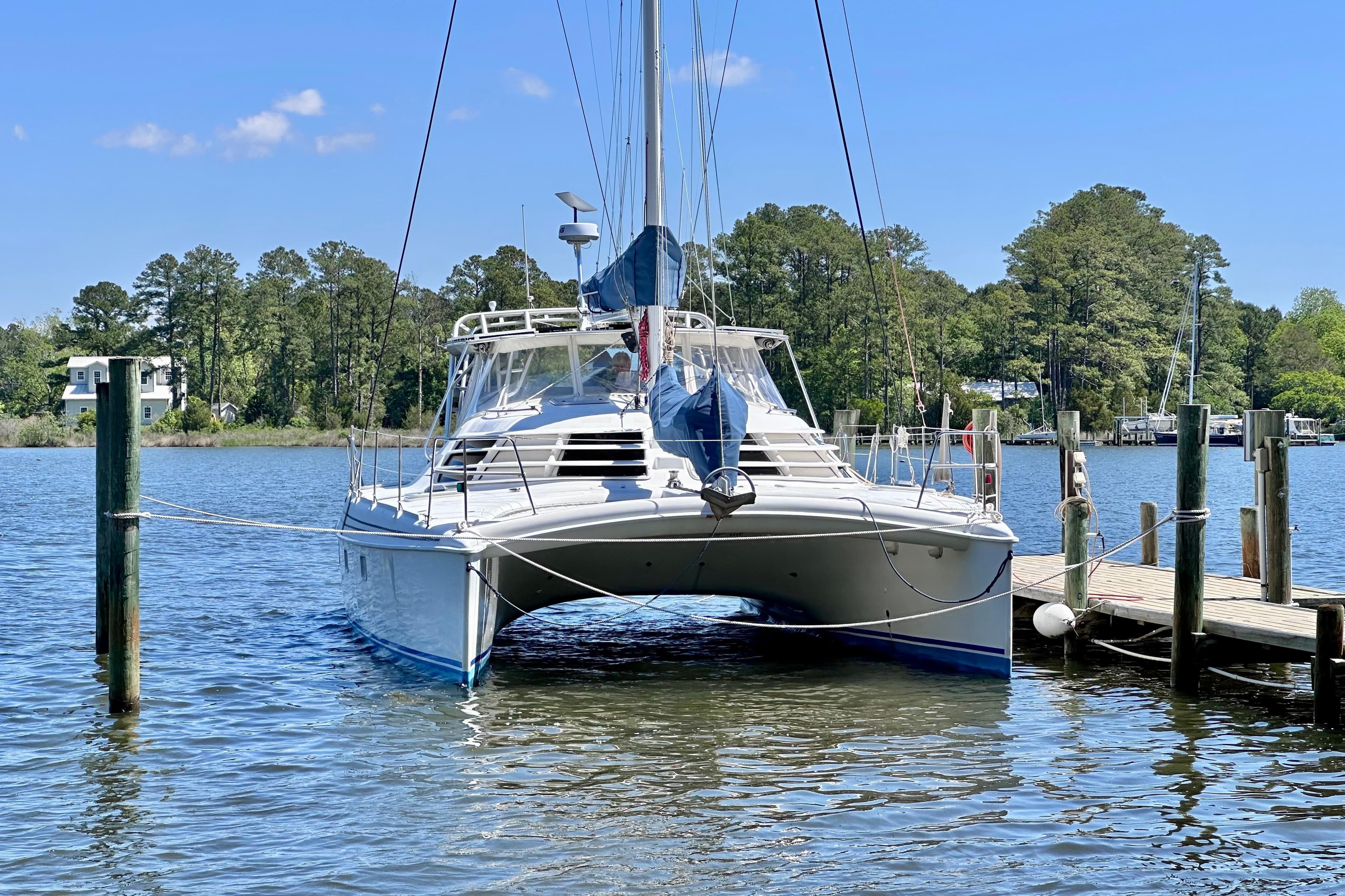 1998 Manta 40 catamaran docked on a serene lake with lush trees.