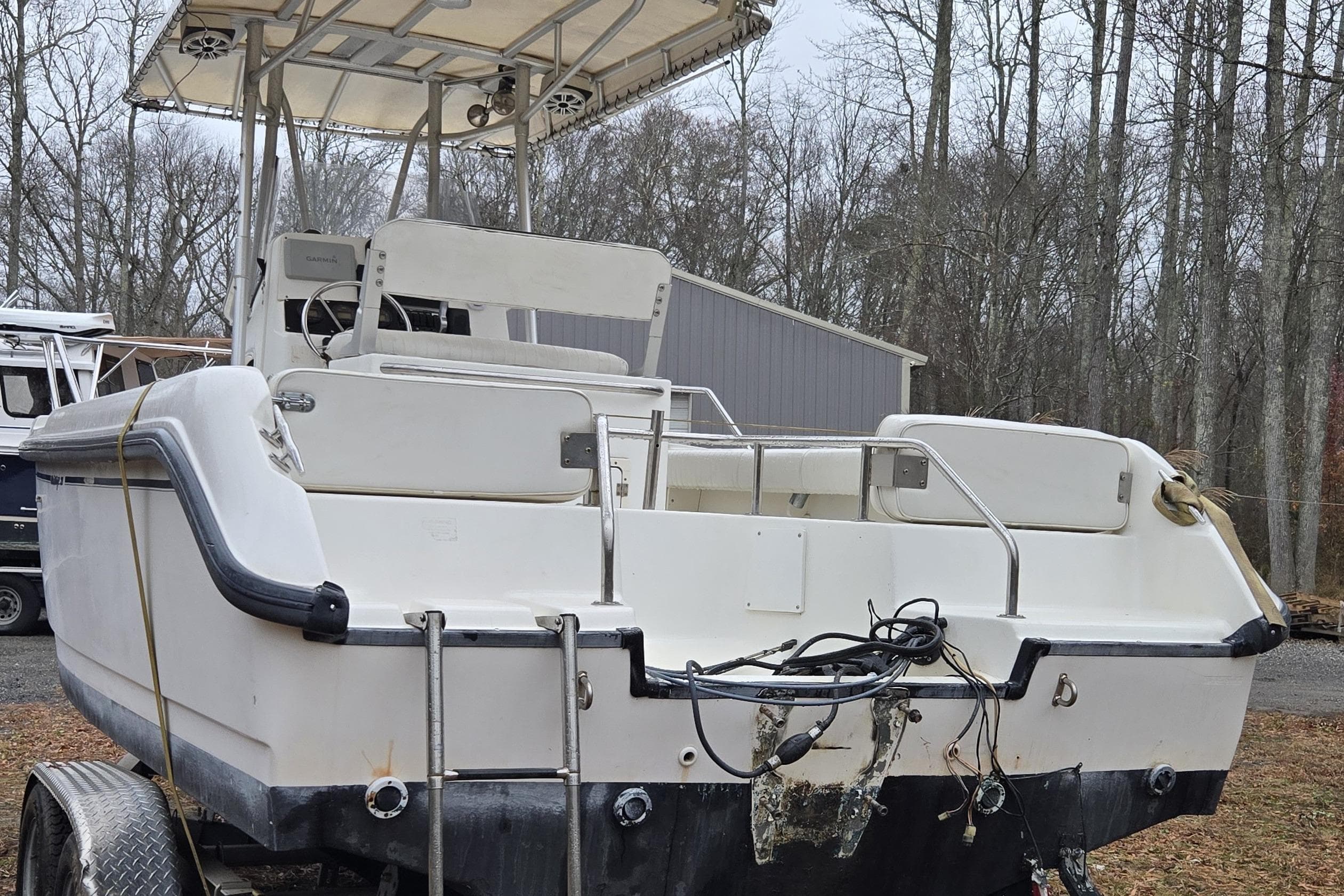 1999 Boston Whaler 21 Outrage boat on trailer, parked outdoors in wooded area.