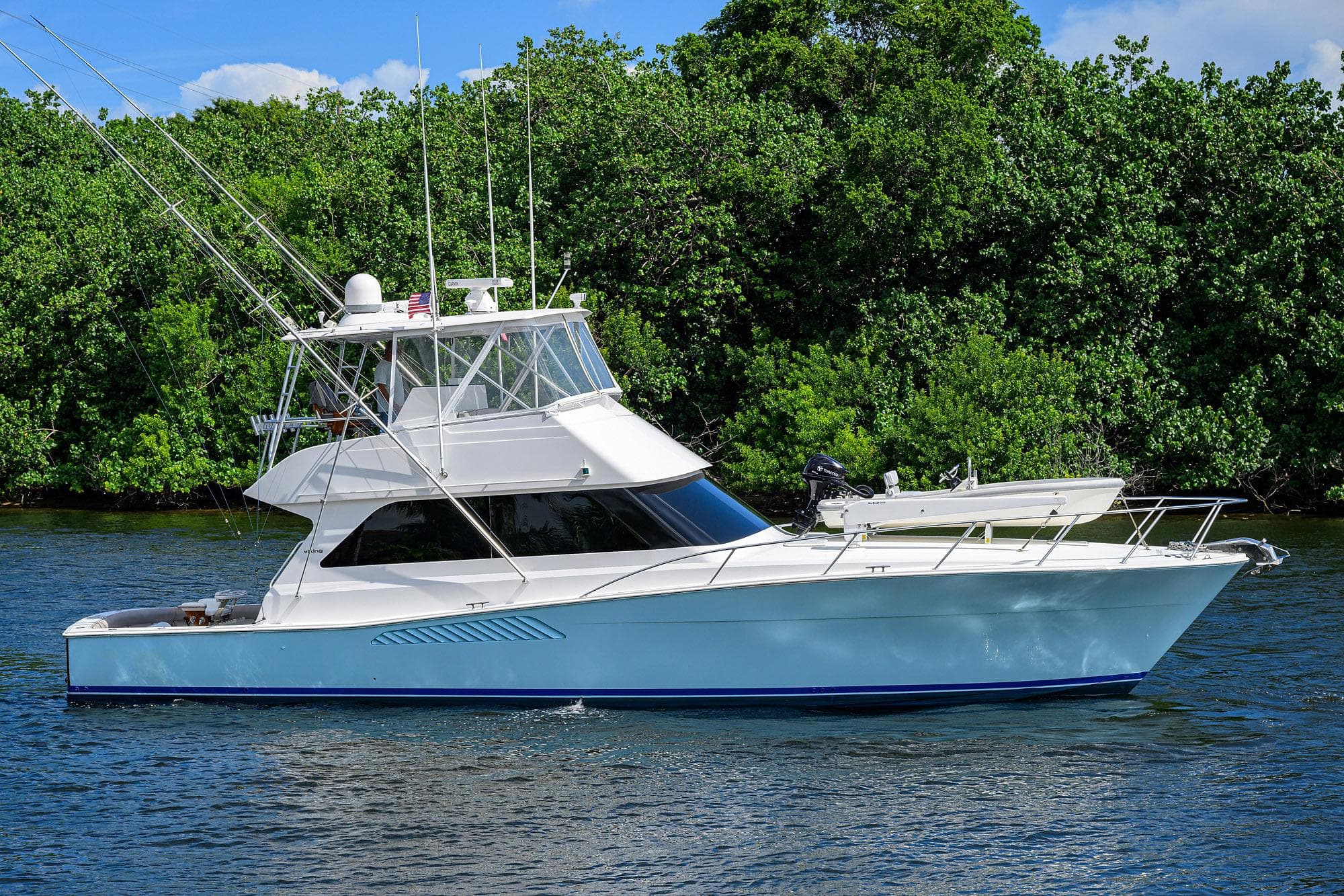Viking 50 Convertible yacht, 2000 model, cruising on a serene waterway with lush greenery.