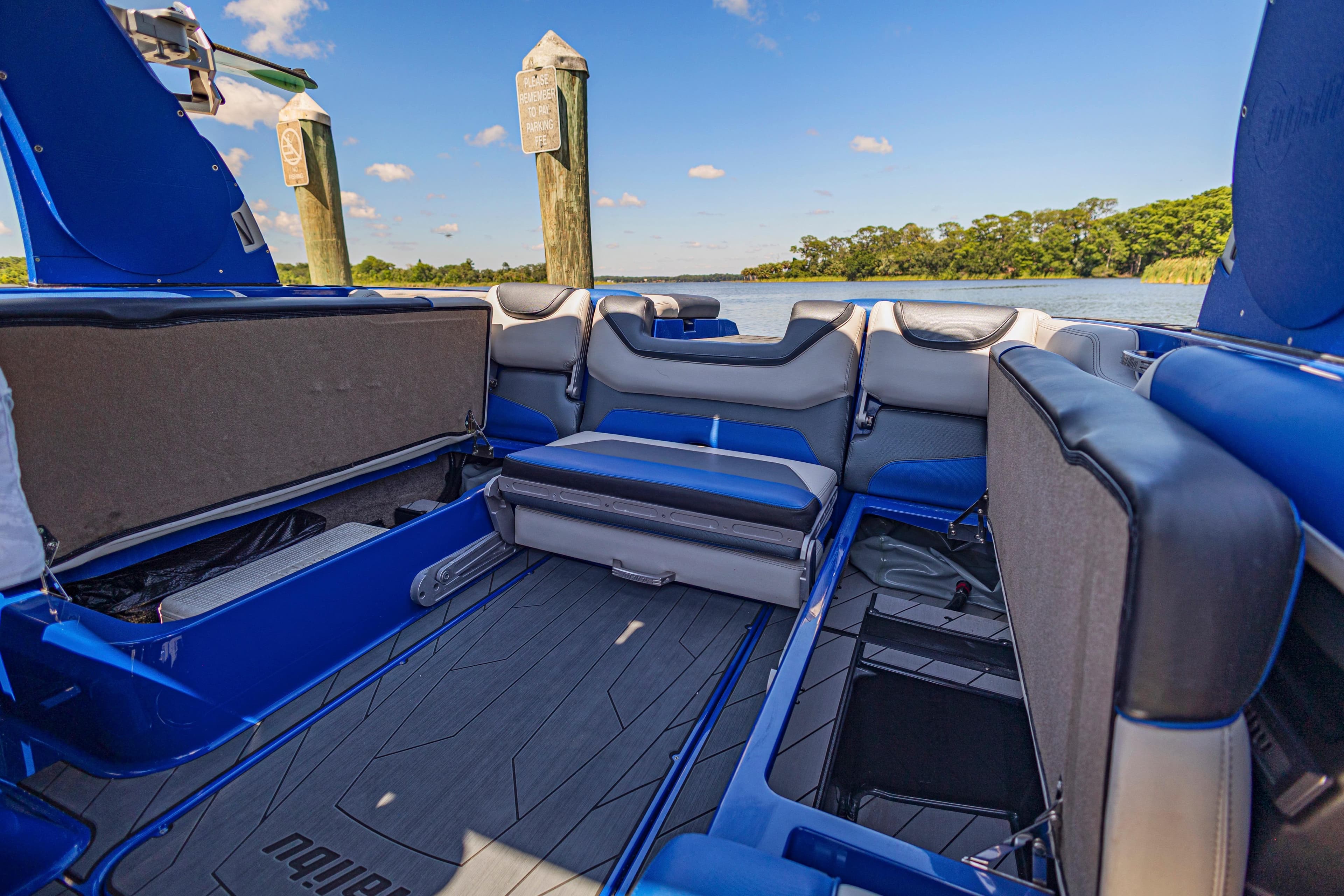 Interior of a 2017 Malibu M235 boat with blue and gray seating, docked by a scenic lake.