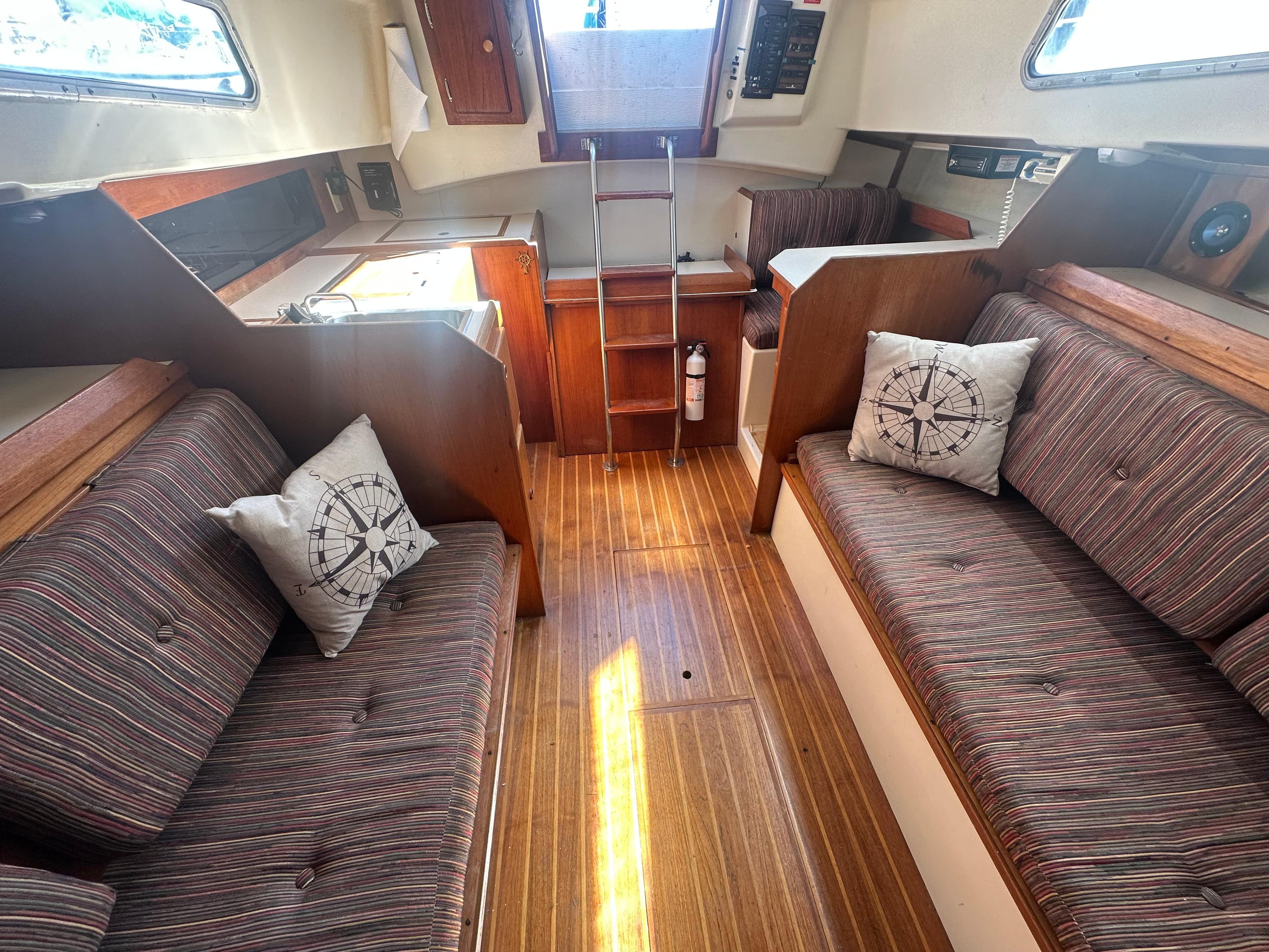 1981 Pearson 32 sailboat interior with striped seating, wooden flooring, and nautical-themed pillows.