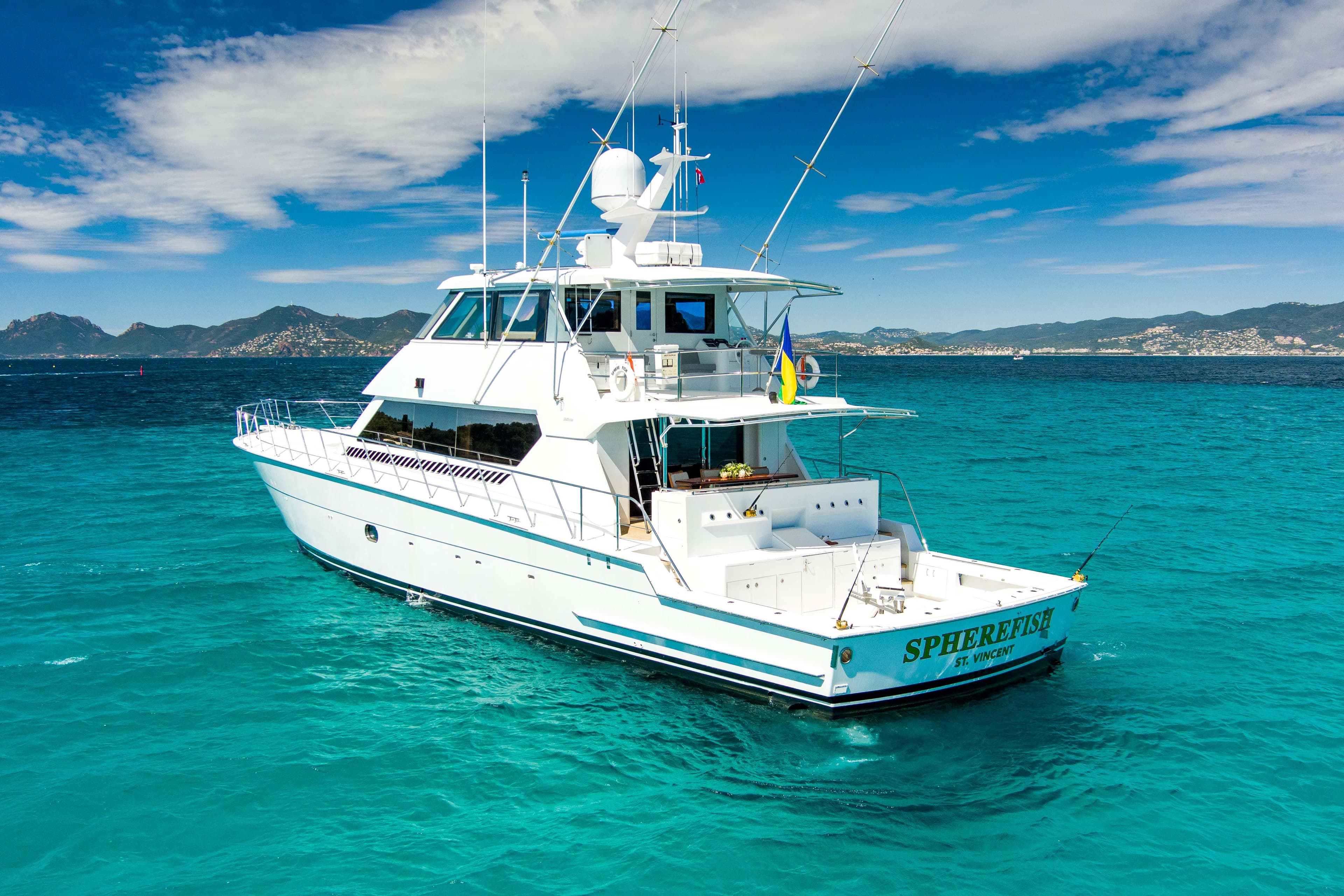 2003 Hatteras 86 Convertible yacht on turquoise waters with scenic mountain backdrop.