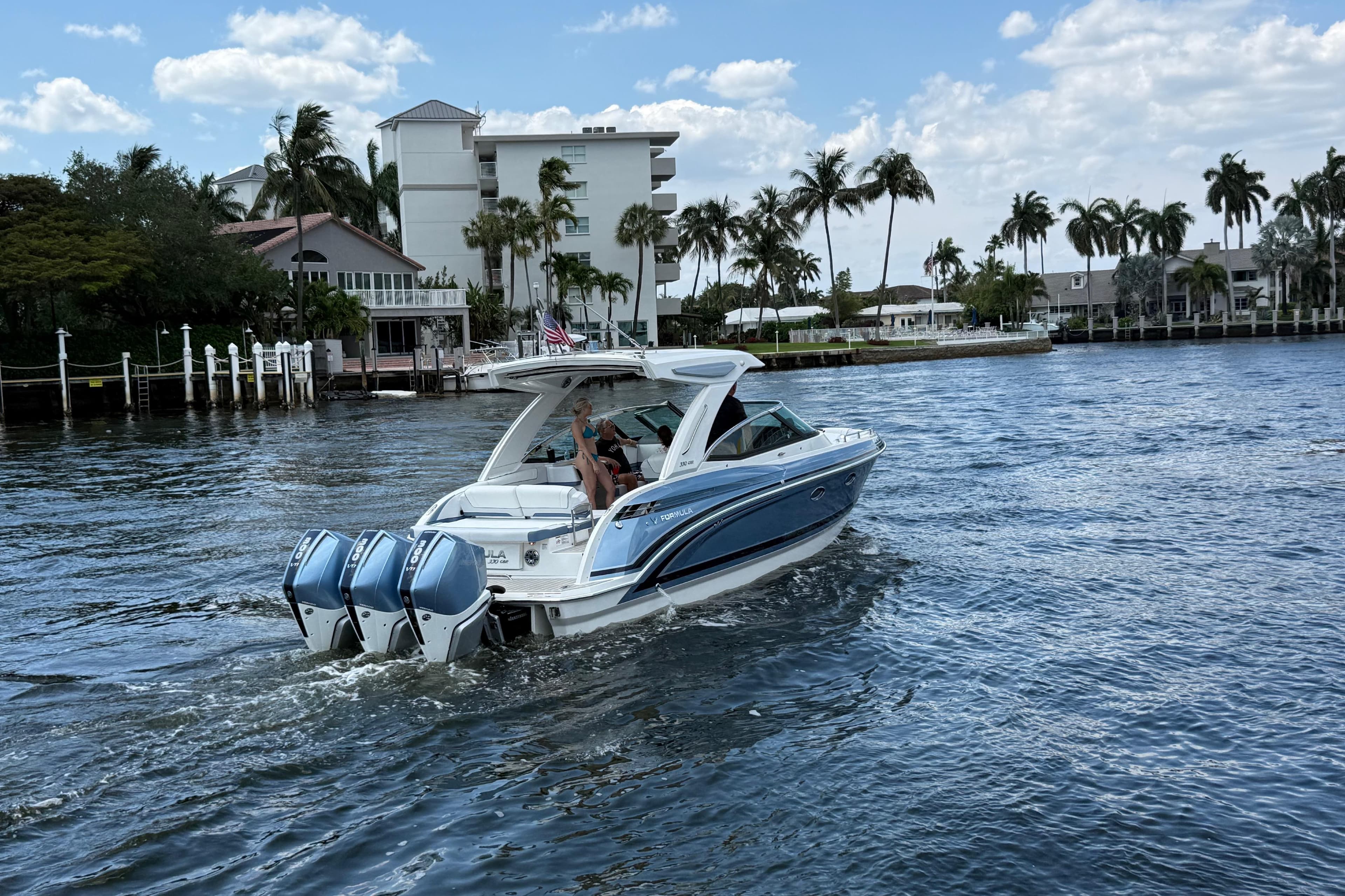 2025 Formula 330 Crossover Bowrider OB cruising on a scenic waterway with palm trees.