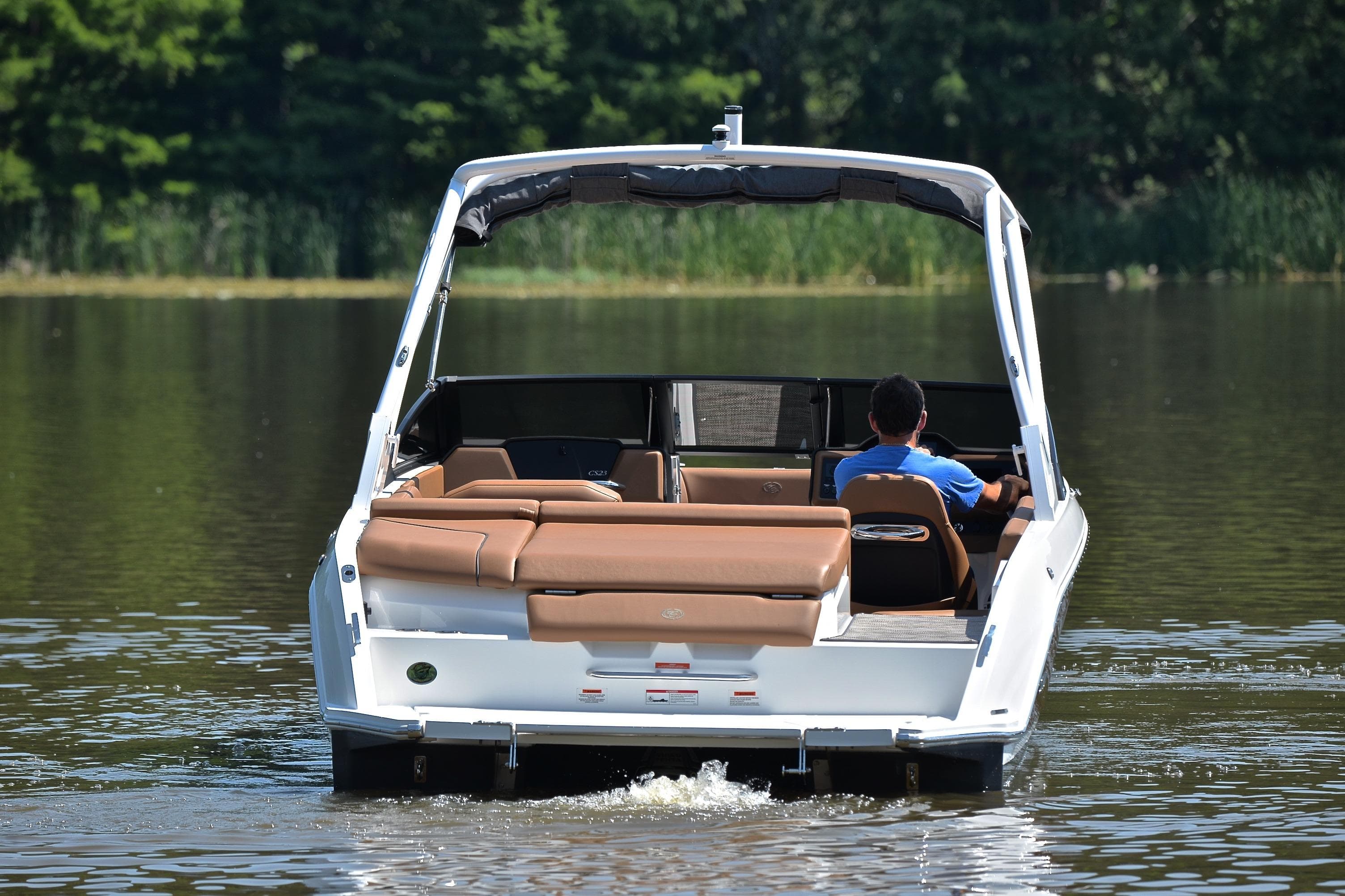 2024 Cobalt CS23 boat cruising on a calm lake with lush greenery.