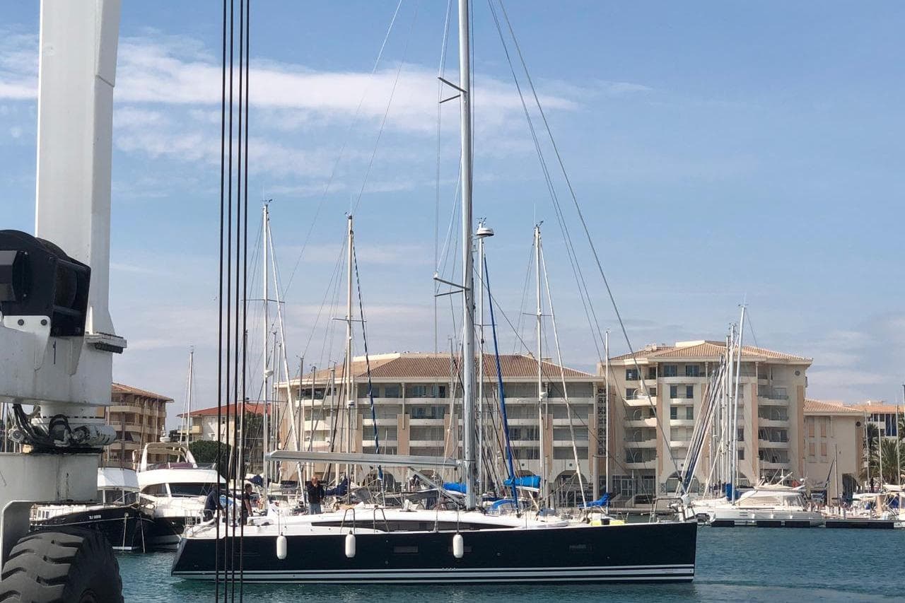 2018 Jeanneau 54 yacht docked in marina with buildings in background.