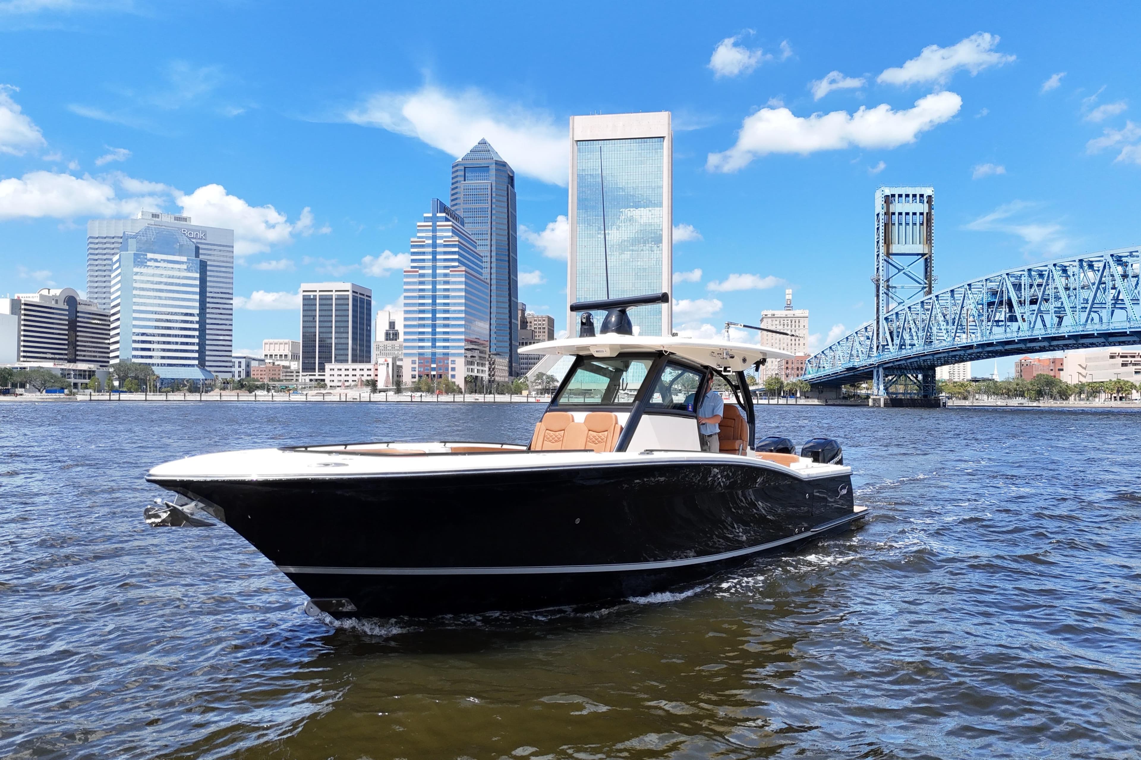 2021 Scout 330 LXF boat cruising near city skyline and blue bridge on a sunny day.