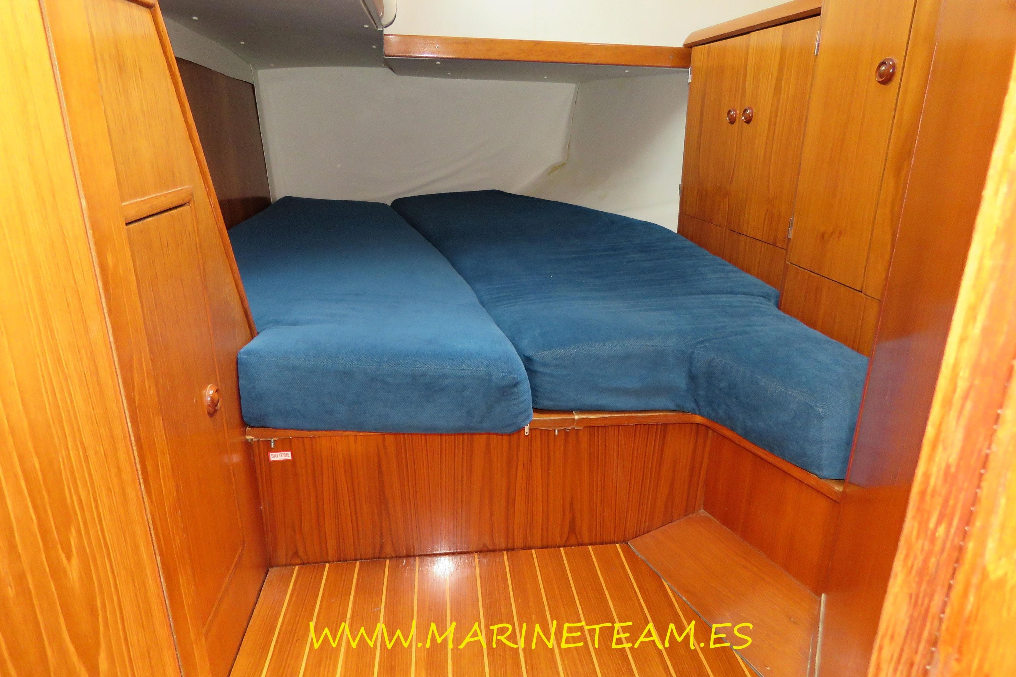 Cozy cabin interior of 1995 Jeanneau Sun Odyssey 45.1 with wooden finish and blue bedding.