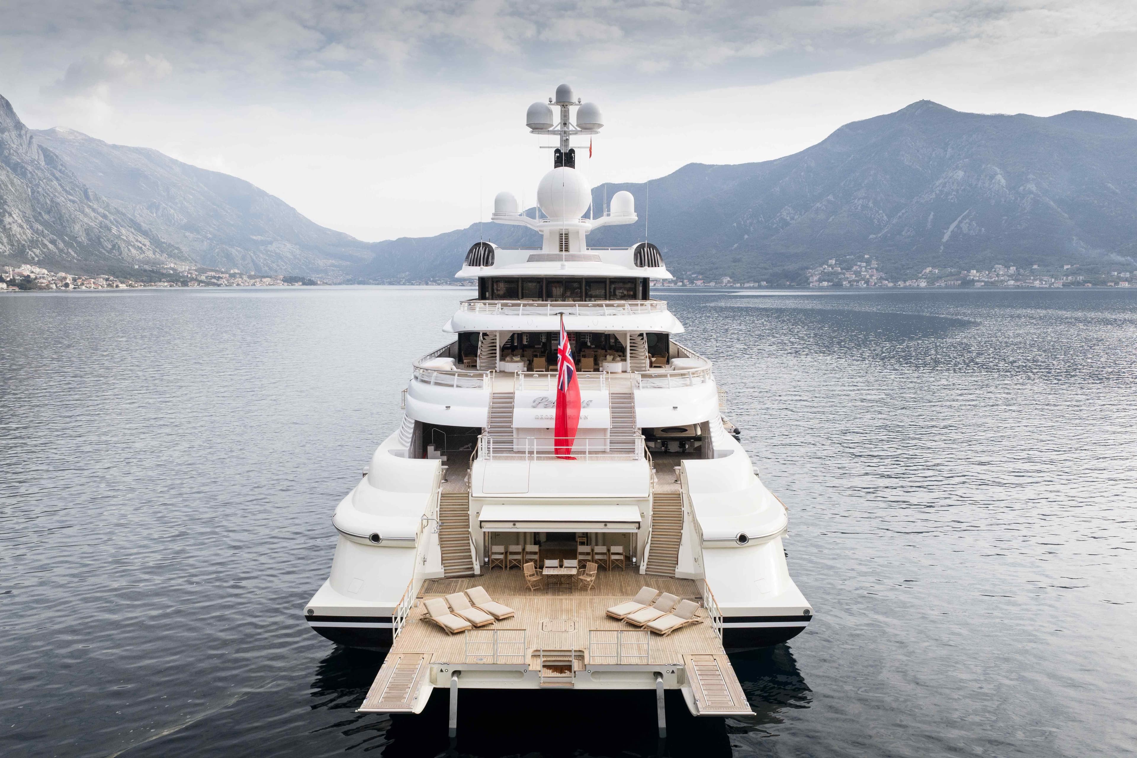 Luxurious 2003 Lurssen custom-built yacht with spacious deck, set against mountainous backdrop.