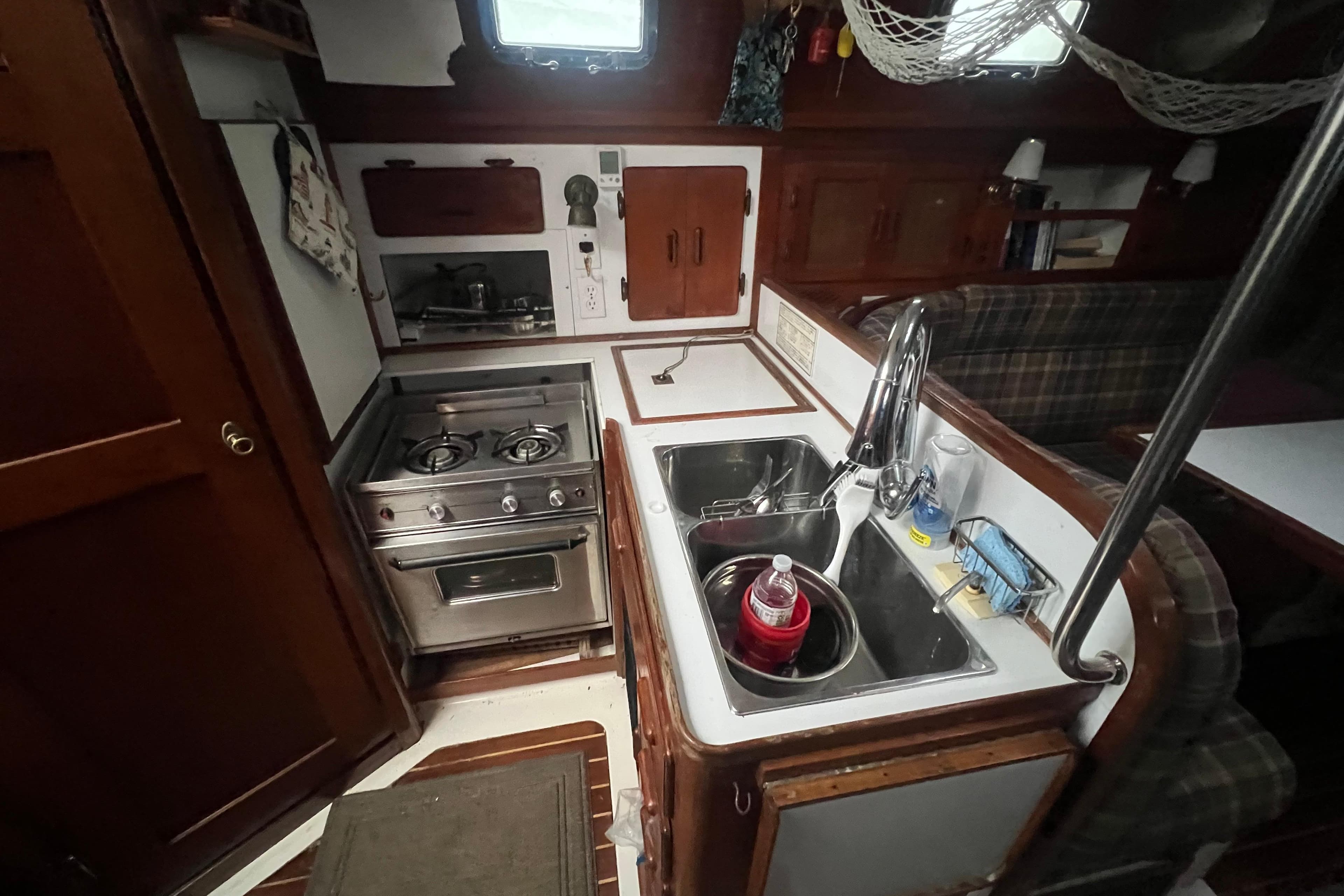 Compact kitchen area in a 1993 Com-Pac Sloop sailboat, featuring stove and sink.