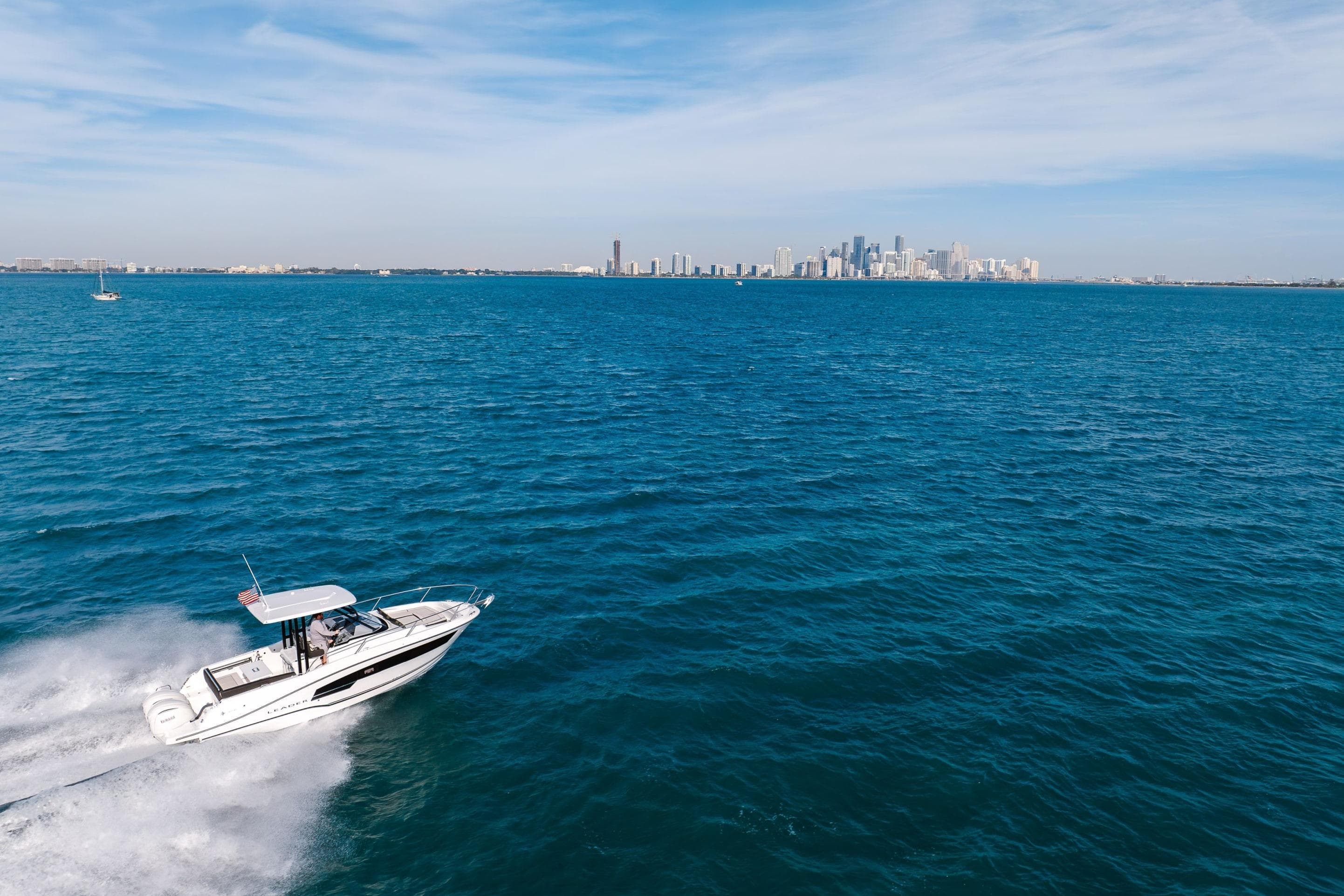 2026 Jeanneau Leader 9.0 WA cruising on blue ocean with city skyline in background.