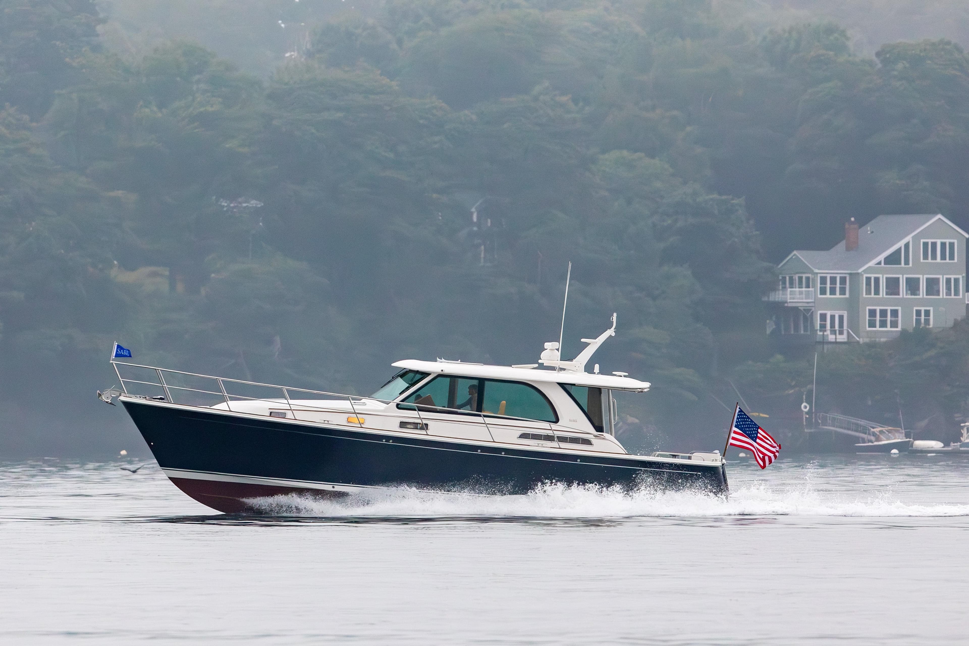 2027 Sabre 45 Salon Express cruising on a misty lake near shoreline homes.