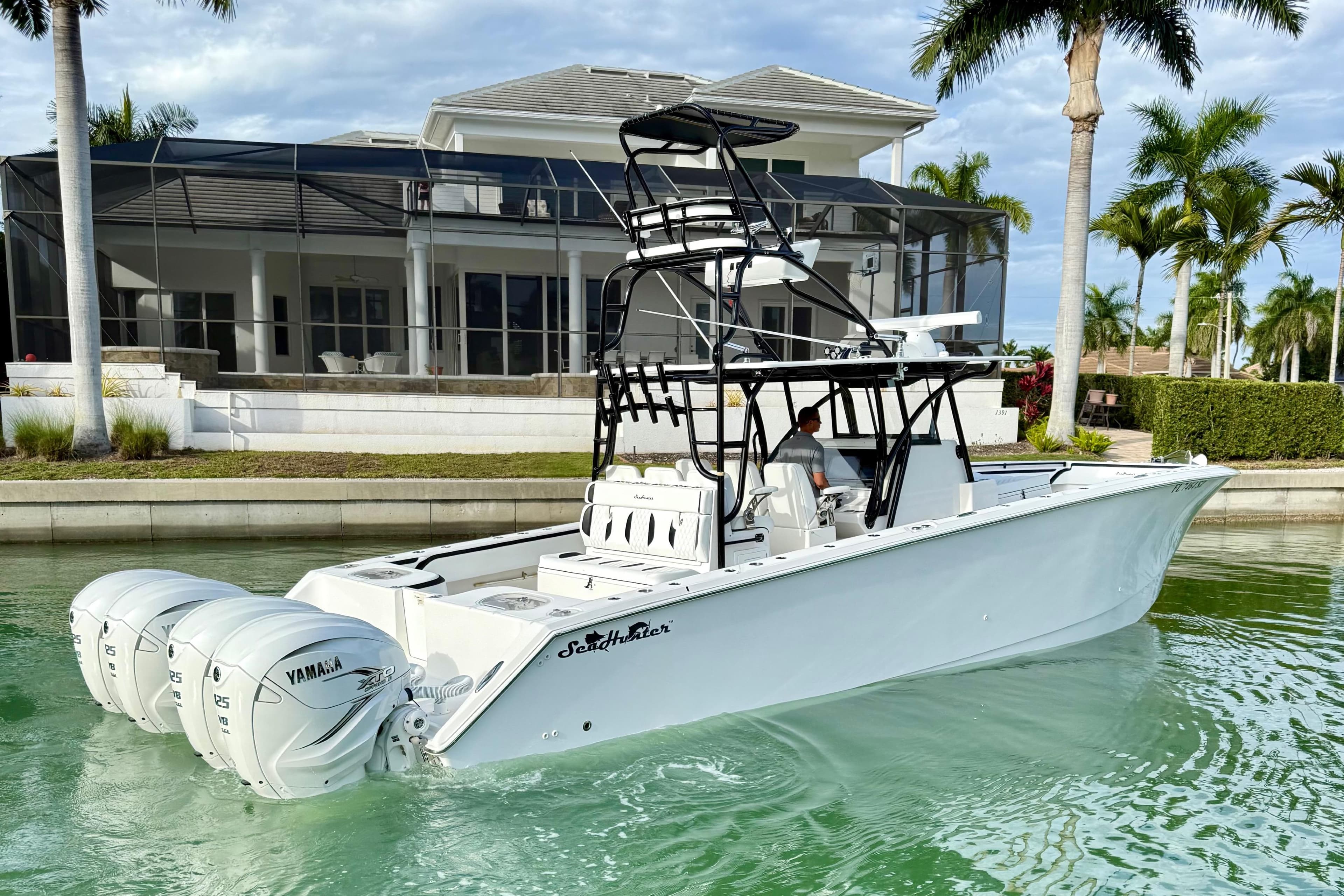 2020 SeaHunter 41 CTS boat with triple Yamaha engines docked near a luxury waterfront home.