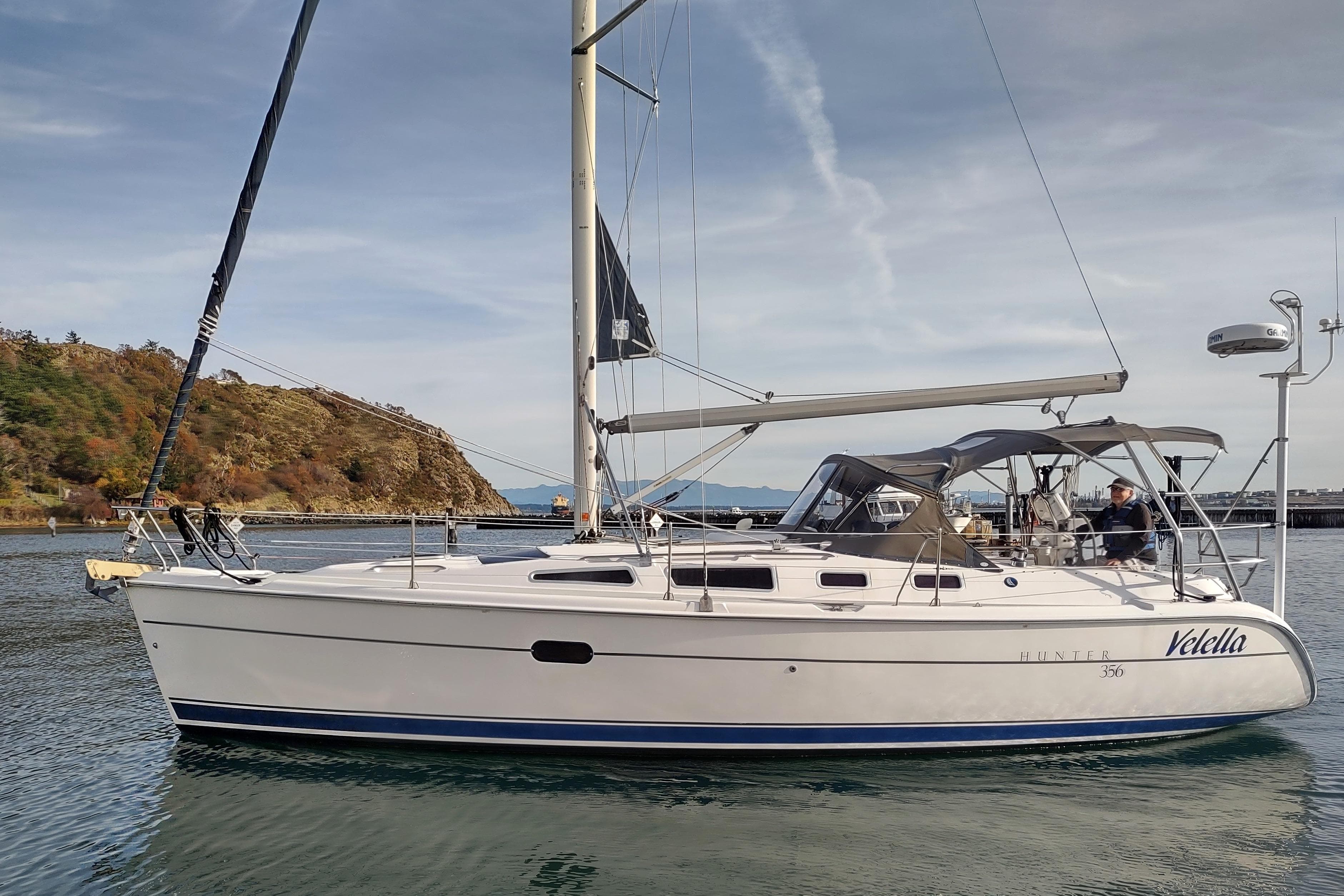 2003 Hunter 356 sailboat on calm water near rocky shoreline.