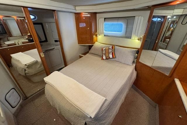 1999 Sea Ray 420 Aft Cabin bedroom with cozy bed, wooden cabinetry, and mirrored closet.
