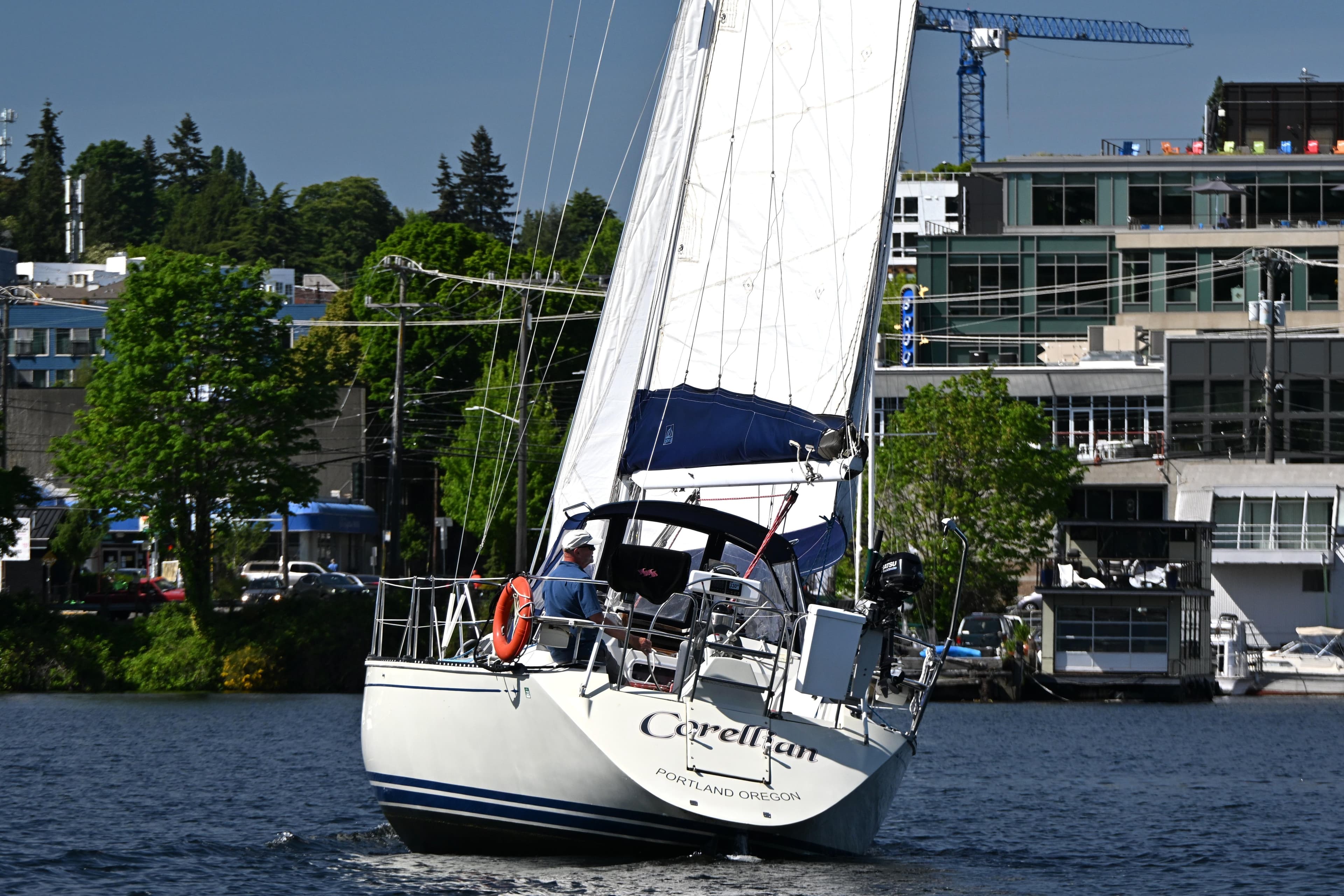 Sailboat C&C 37/40+ (1989) navigating urban waters with lush greenery and buildings in the background.