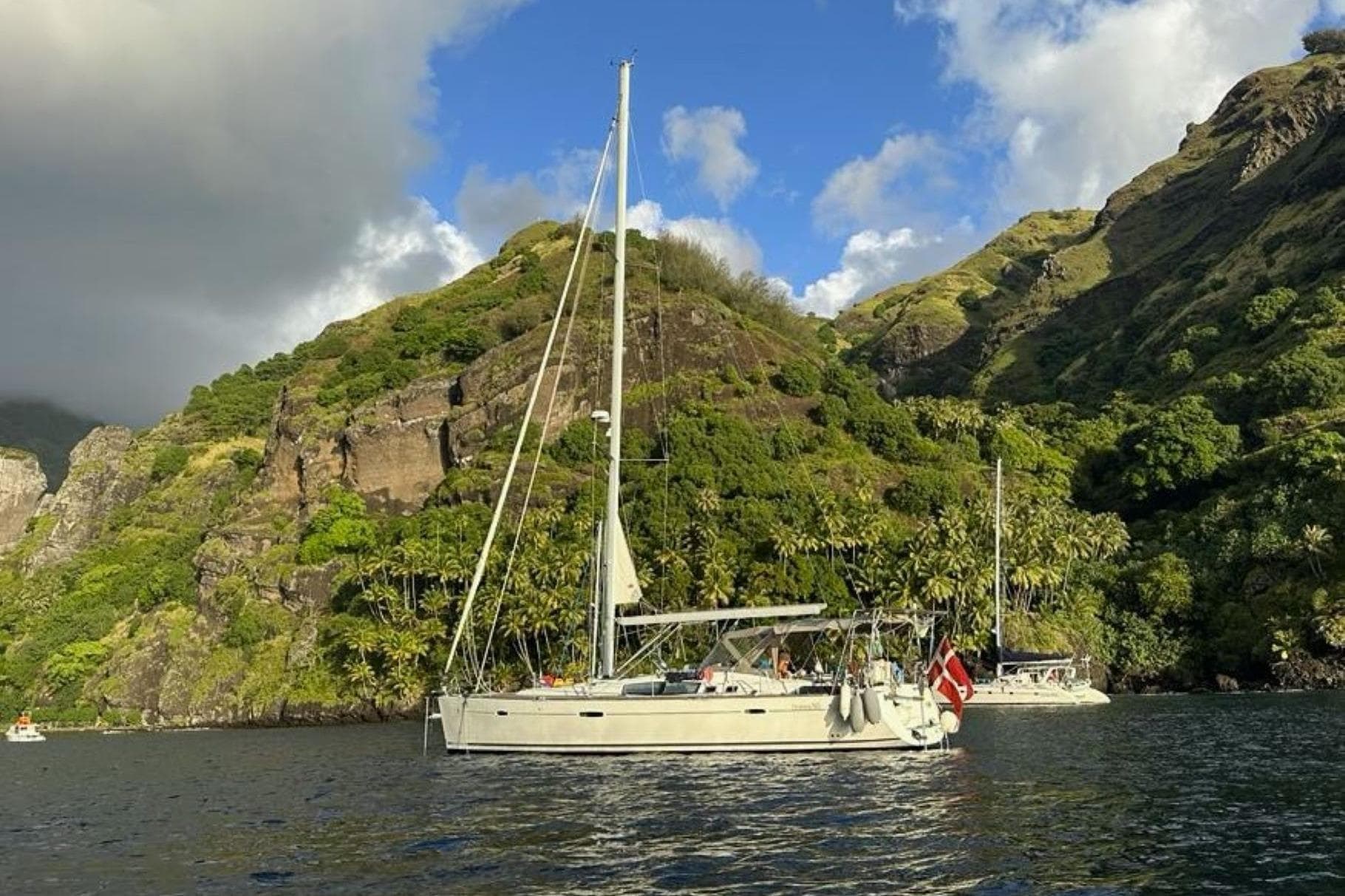 2008 Beneteau Oceanis 50 sailboat anchored near lush, mountainous coastline.