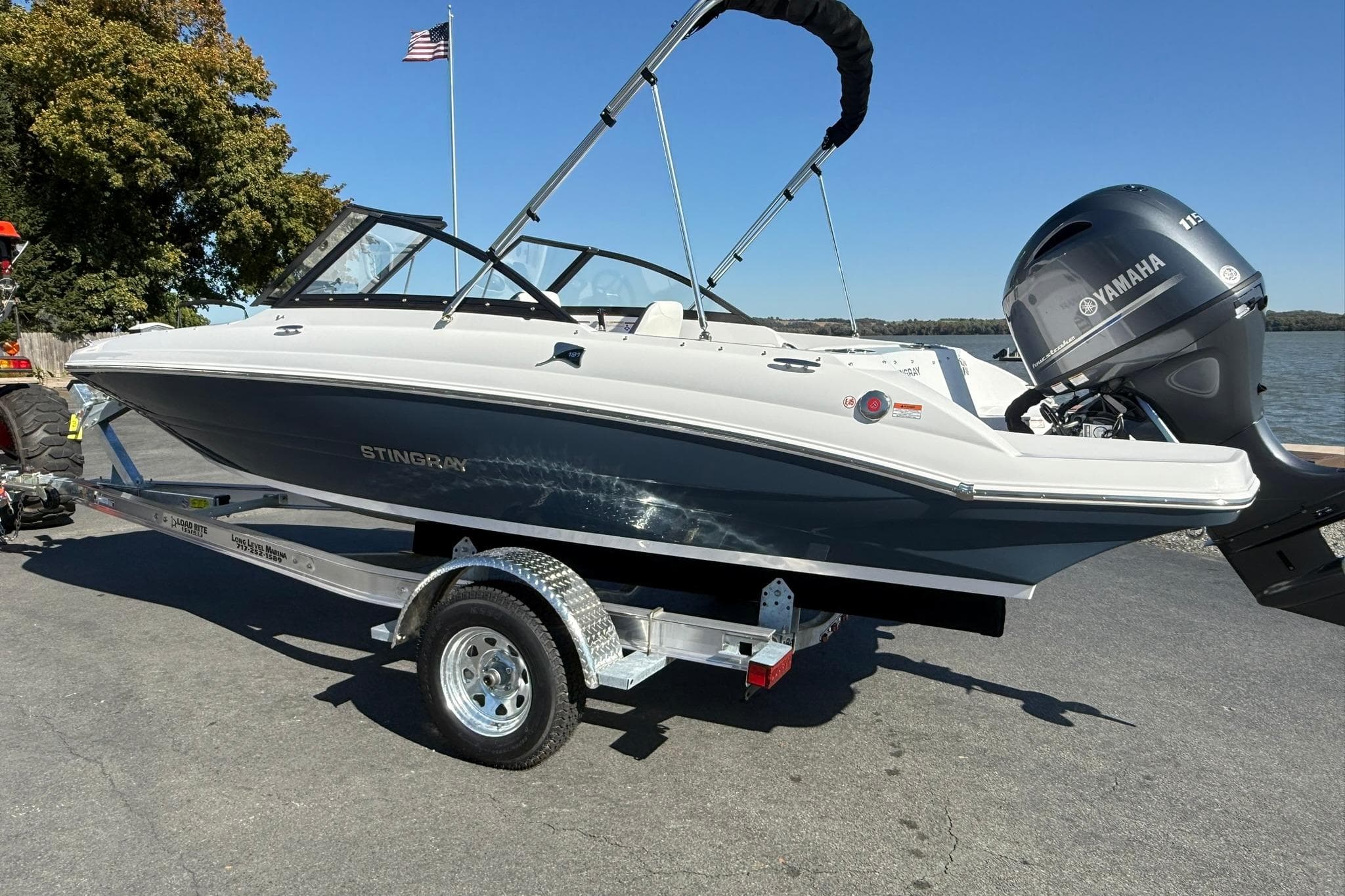 2026 Stingray 191 DC boat on trailer with Yamaha engine, near water and American flag.