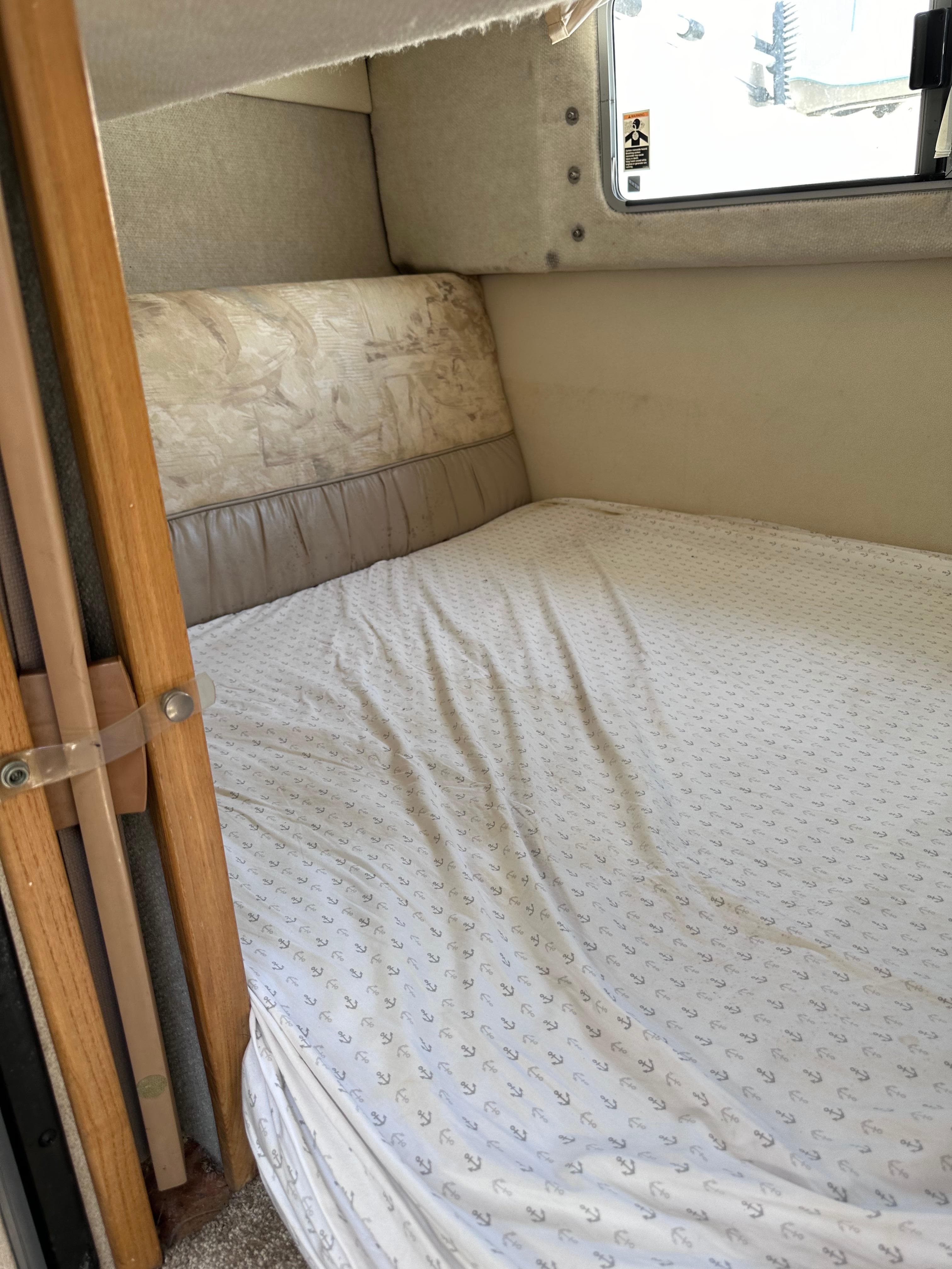 Interior cabin bed of a 1996 Maxum 2400 SCR boat with anchor-patterned sheets.