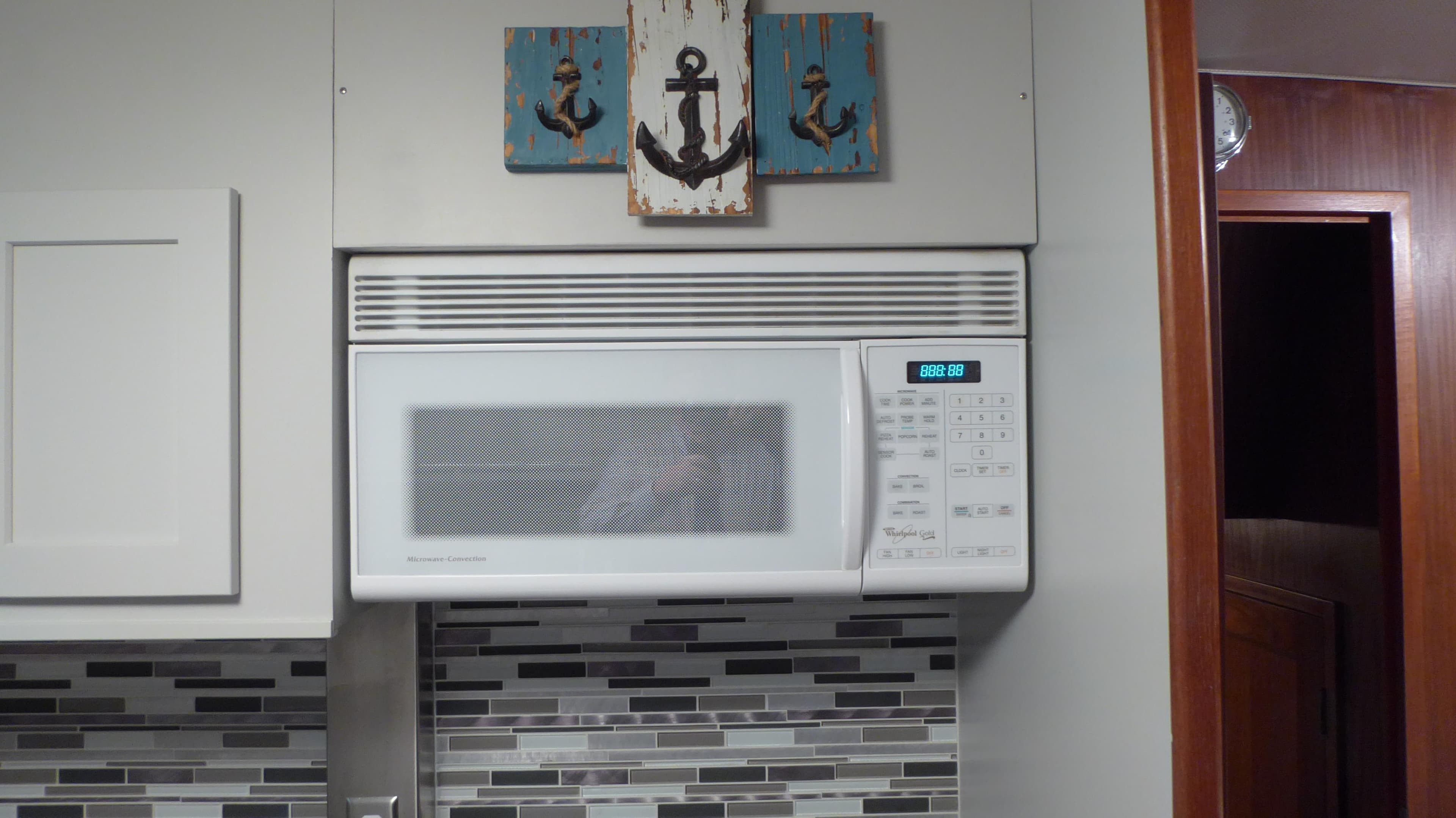 White microwave in yacht kitchen with nautical decor and tiled backsplash.
