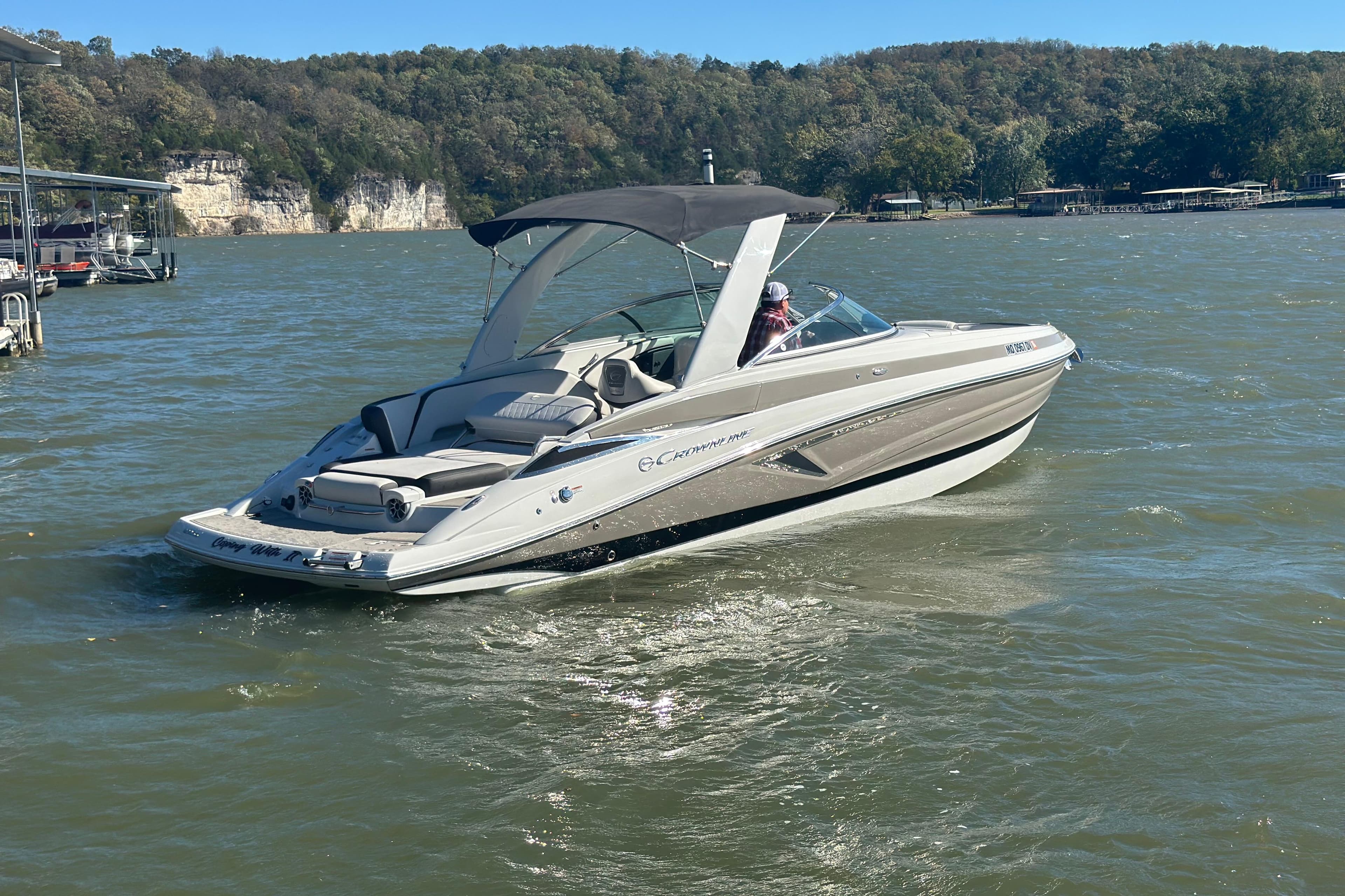 2023 Crownline 290 CR boat cruising on a scenic lake with forested hills.