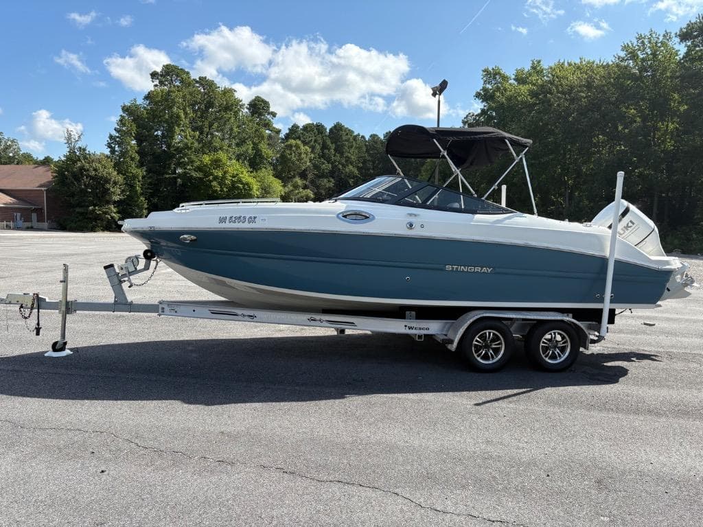 2021 Stingray 231 DC boat on trailer in parking lot, surrounded by trees.