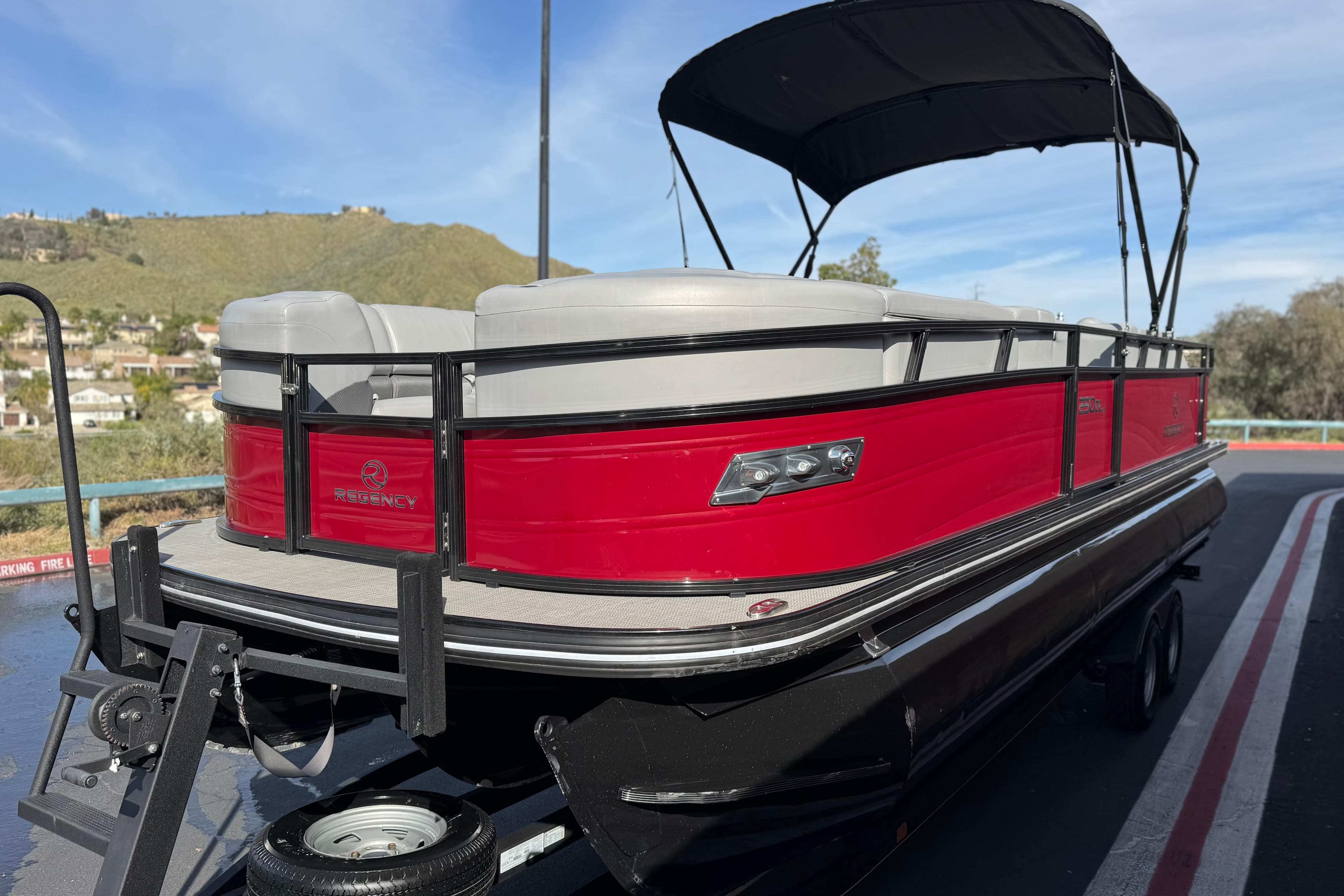 2023 Regency 250 DL3 pontoon boat with red exterior and canopy, parked on a trailer.