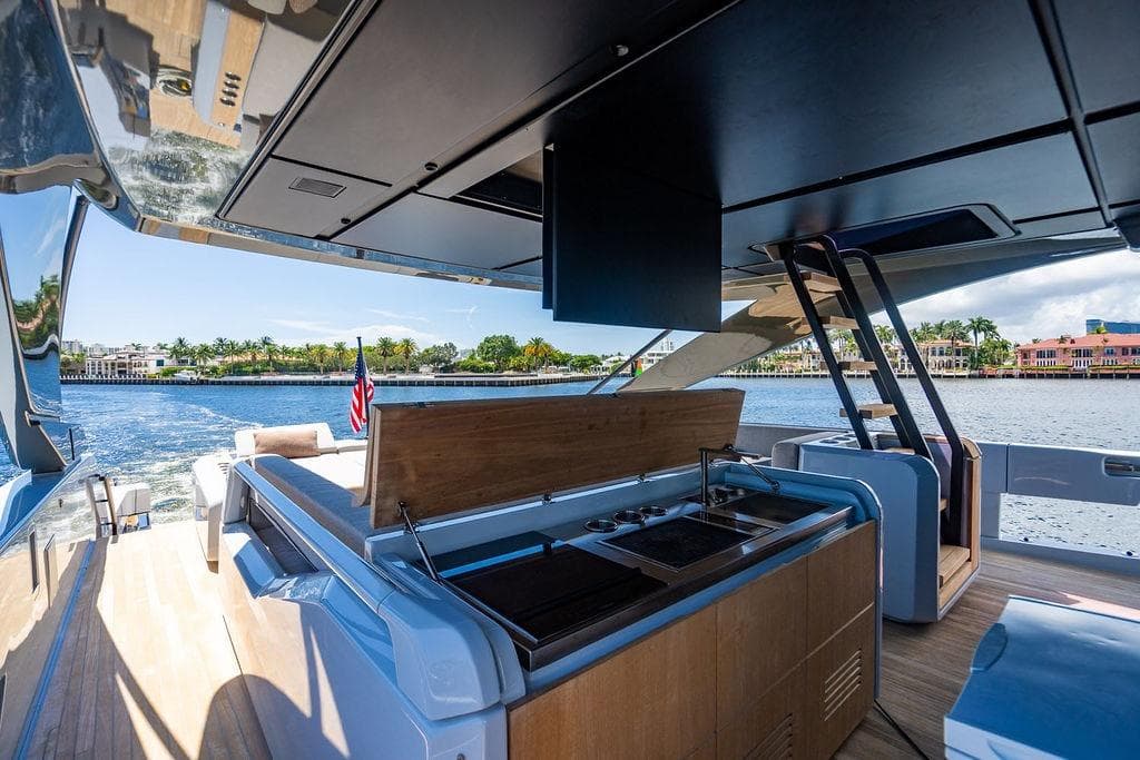 Luxurious 2023 Bluegame BG 72 yacht with outdoor kitchen, cruising on scenic waterfront.