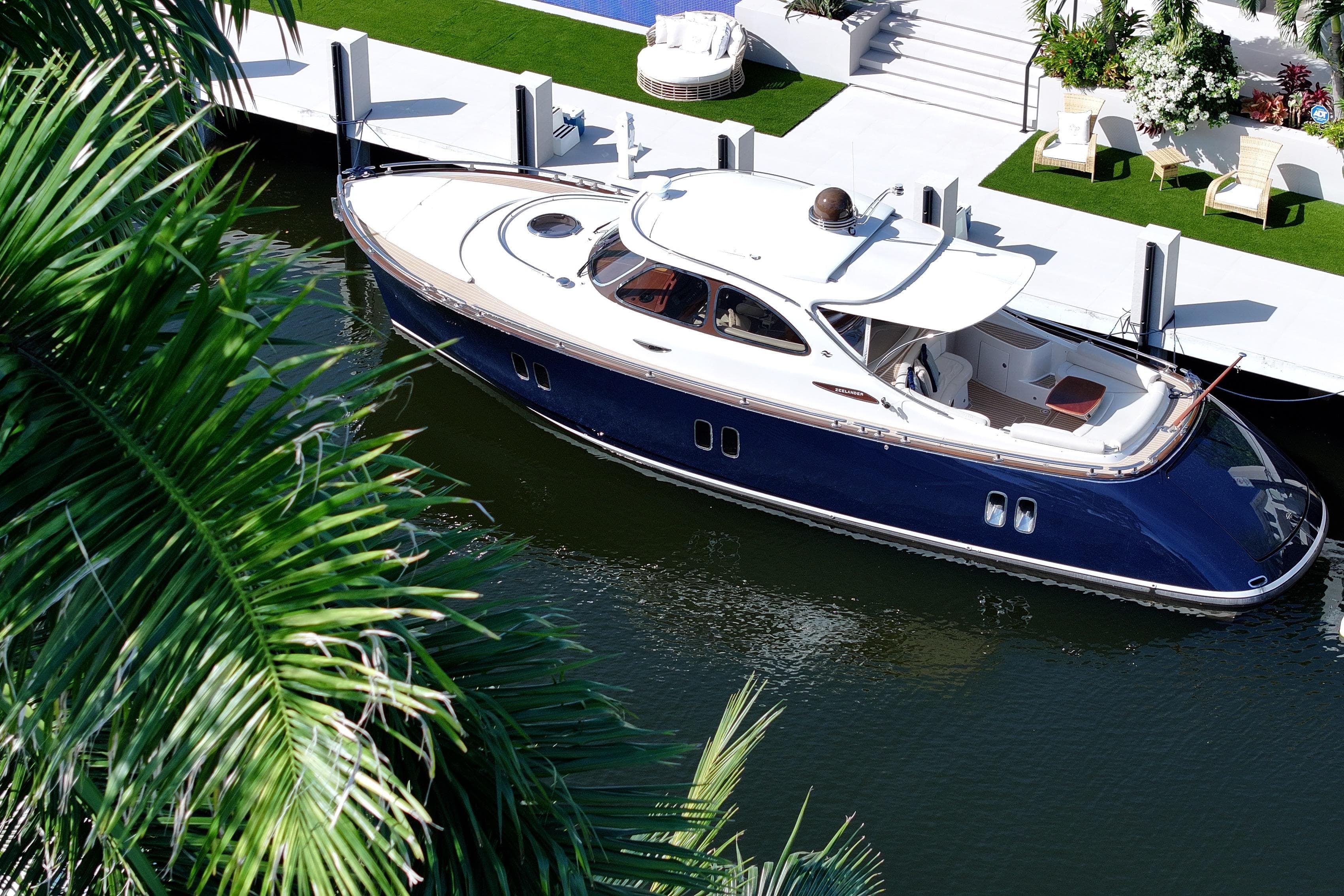 2013 Zeelander Z44 yacht docked by a luxurious waterfront, surrounded by lush greenery.
