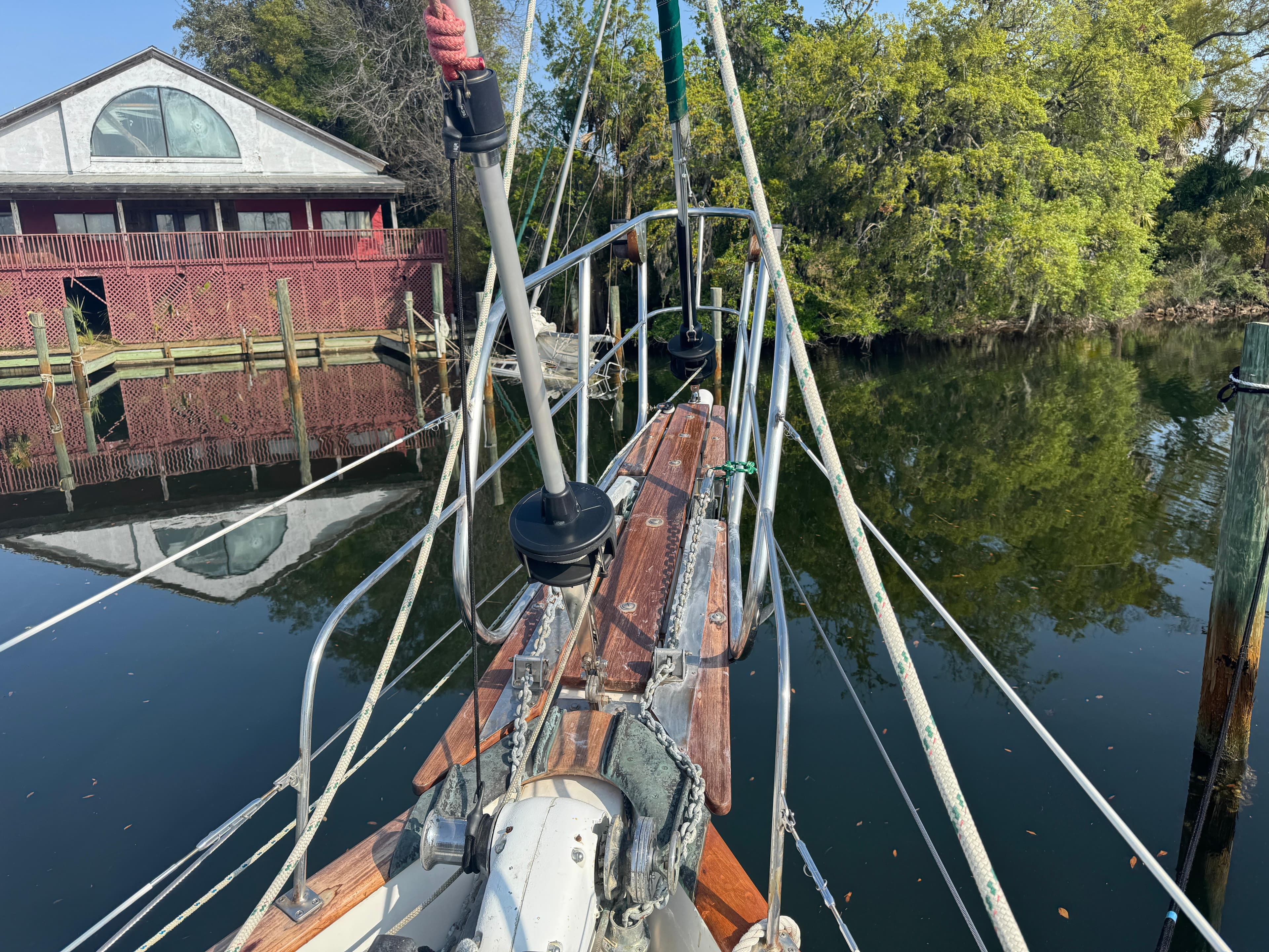 Bow of 1989 Hans Christian 43T sailboat docked near a brick building and trees.