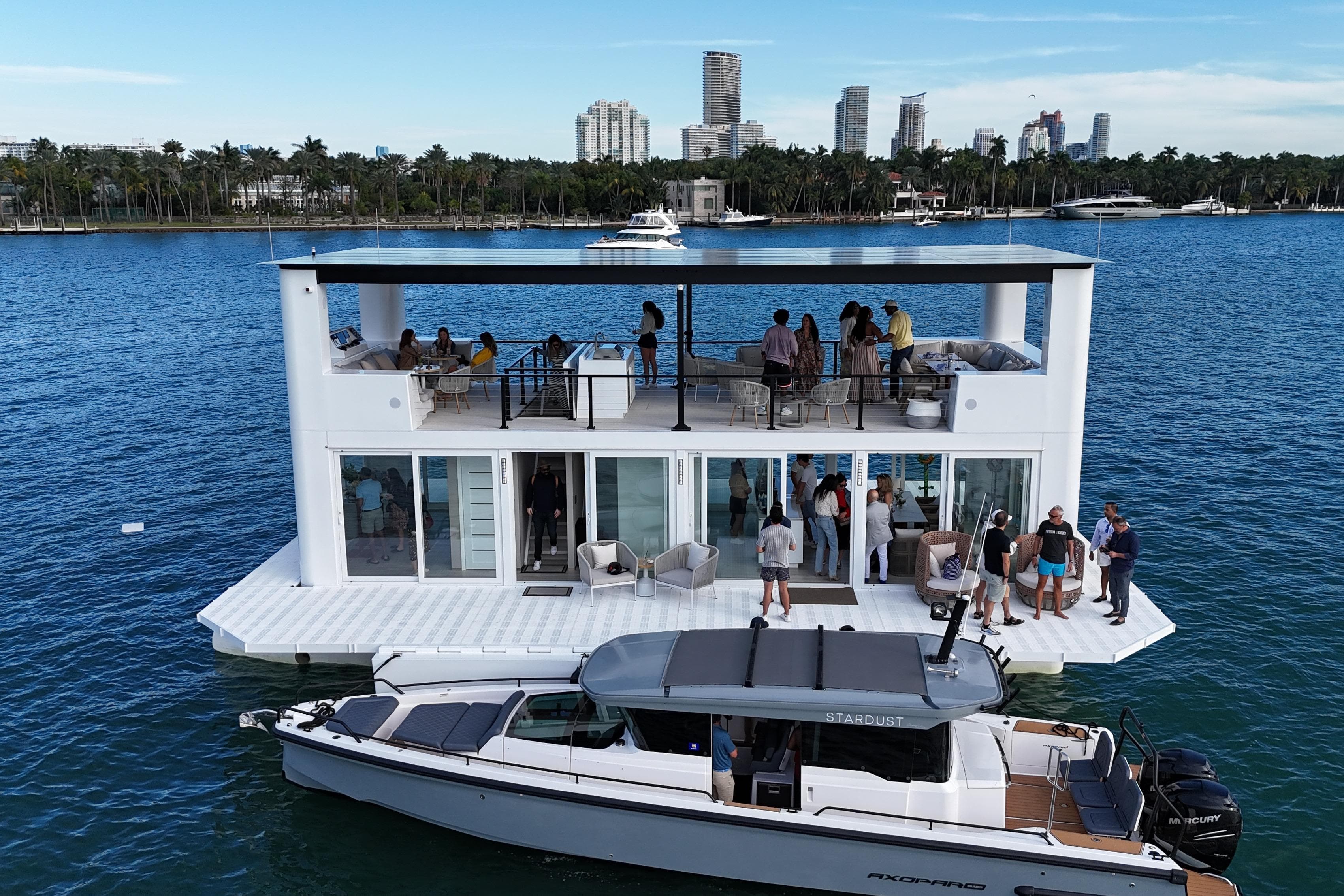 Floating ARKHAUS Villa 50, 2025 model, with people enjoying rooftop and deck, city skyline backdrop.