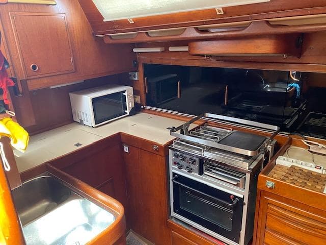 1981 Nautor Swan 51 yacht kitchen with stove, microwave, and wooden cabinetry.