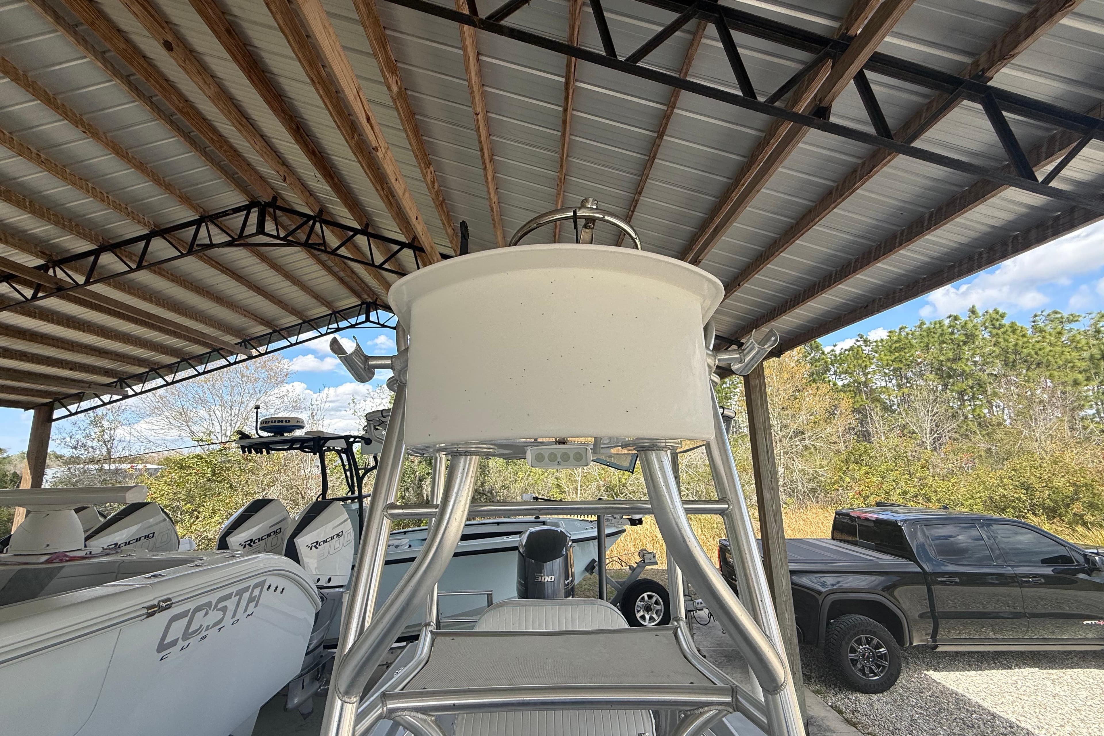 1974 Aquasport 2400 Center Console boat under a metal canopy, surrounded by trees and vehicles.