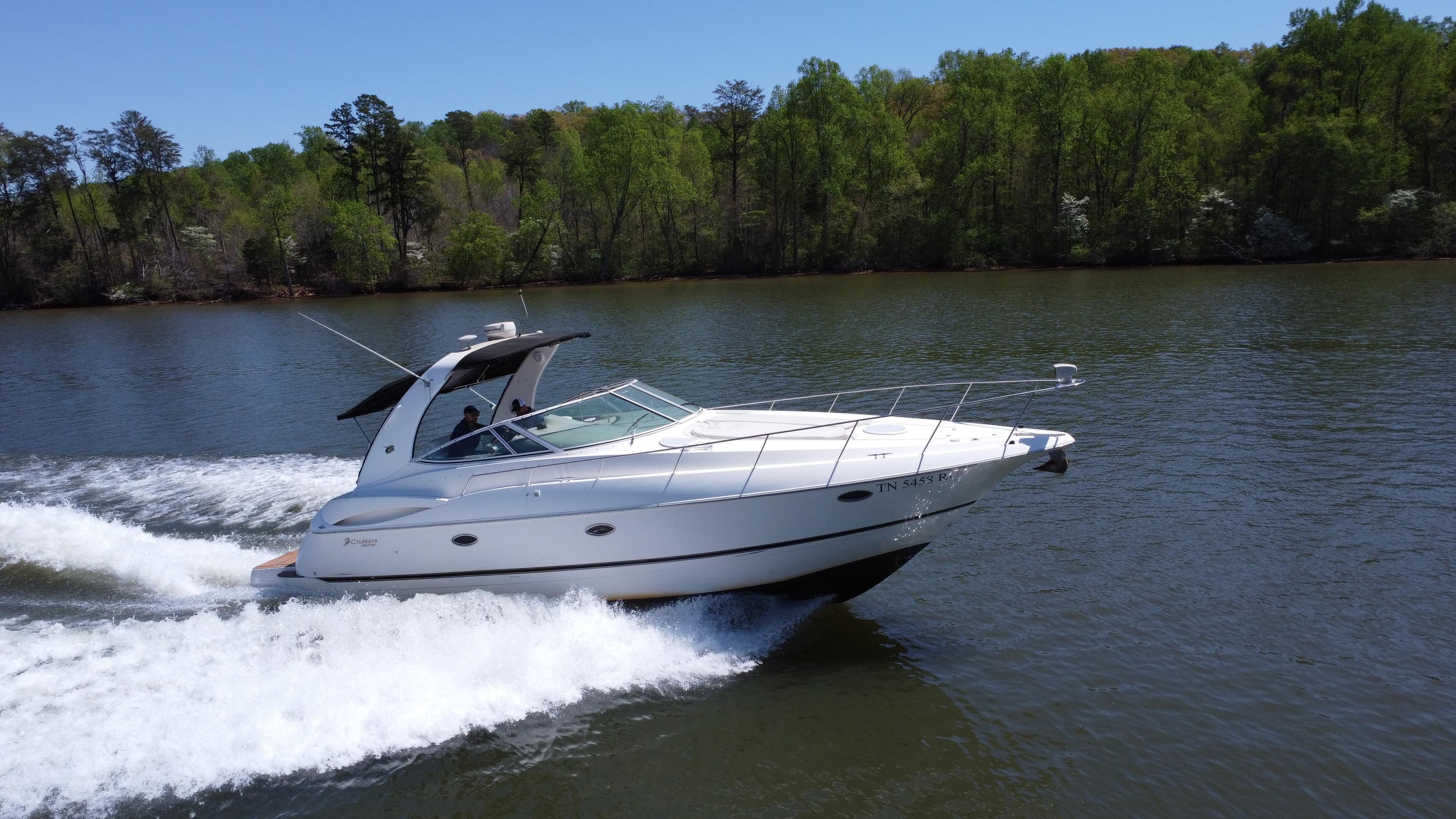 2004 Cruisers Yachts 370 Express speeding on a lake with lush green trees.