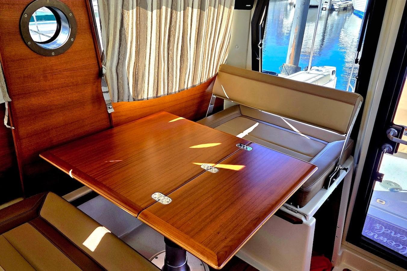 Interior of 2022 Ranger Tugs R-27 with wooden table and seating, dockside view.
