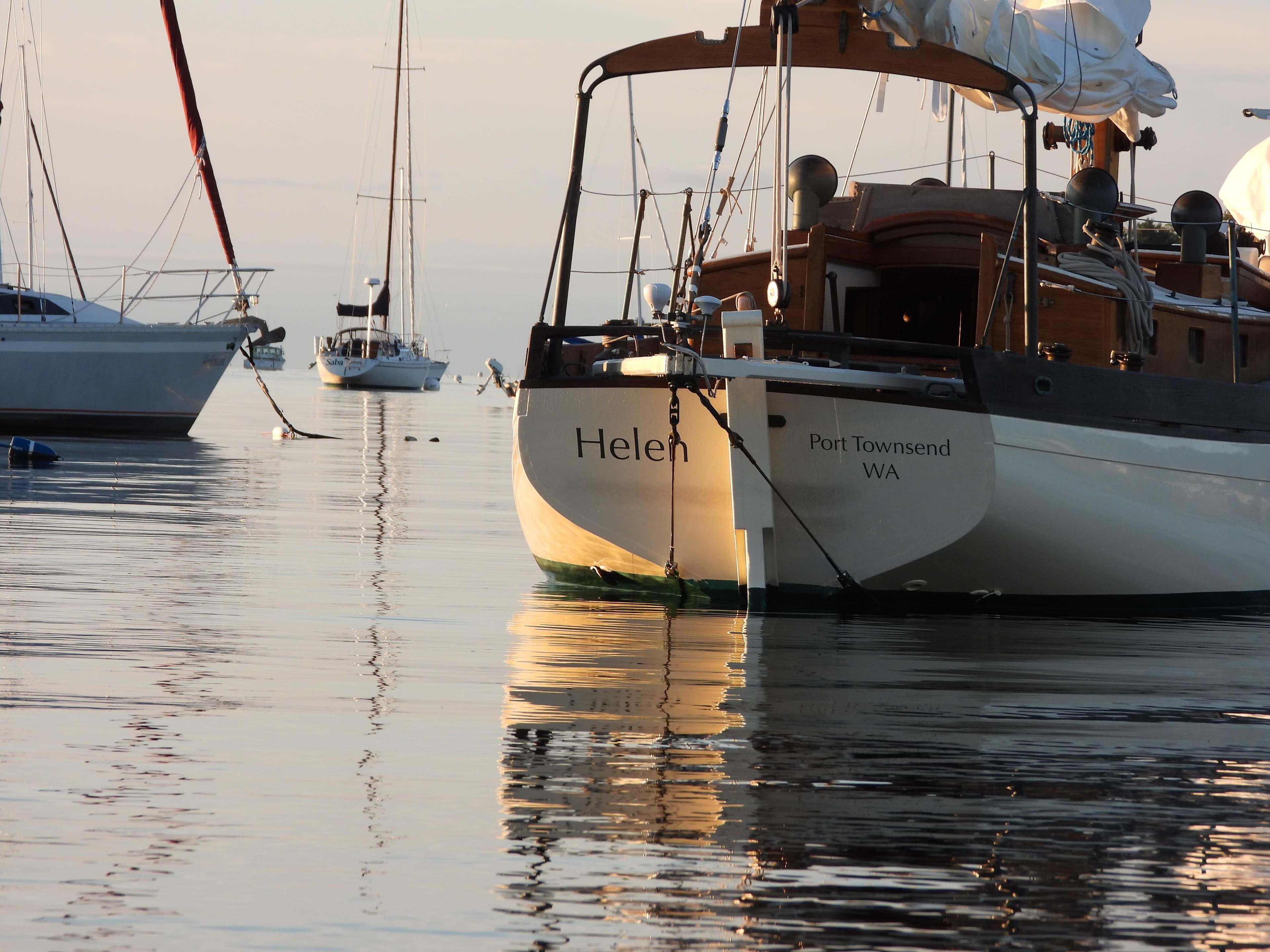 Sailboats anchored on calm water, featuring a 1999 Custom Lyle Hess Cutter named "Helen."