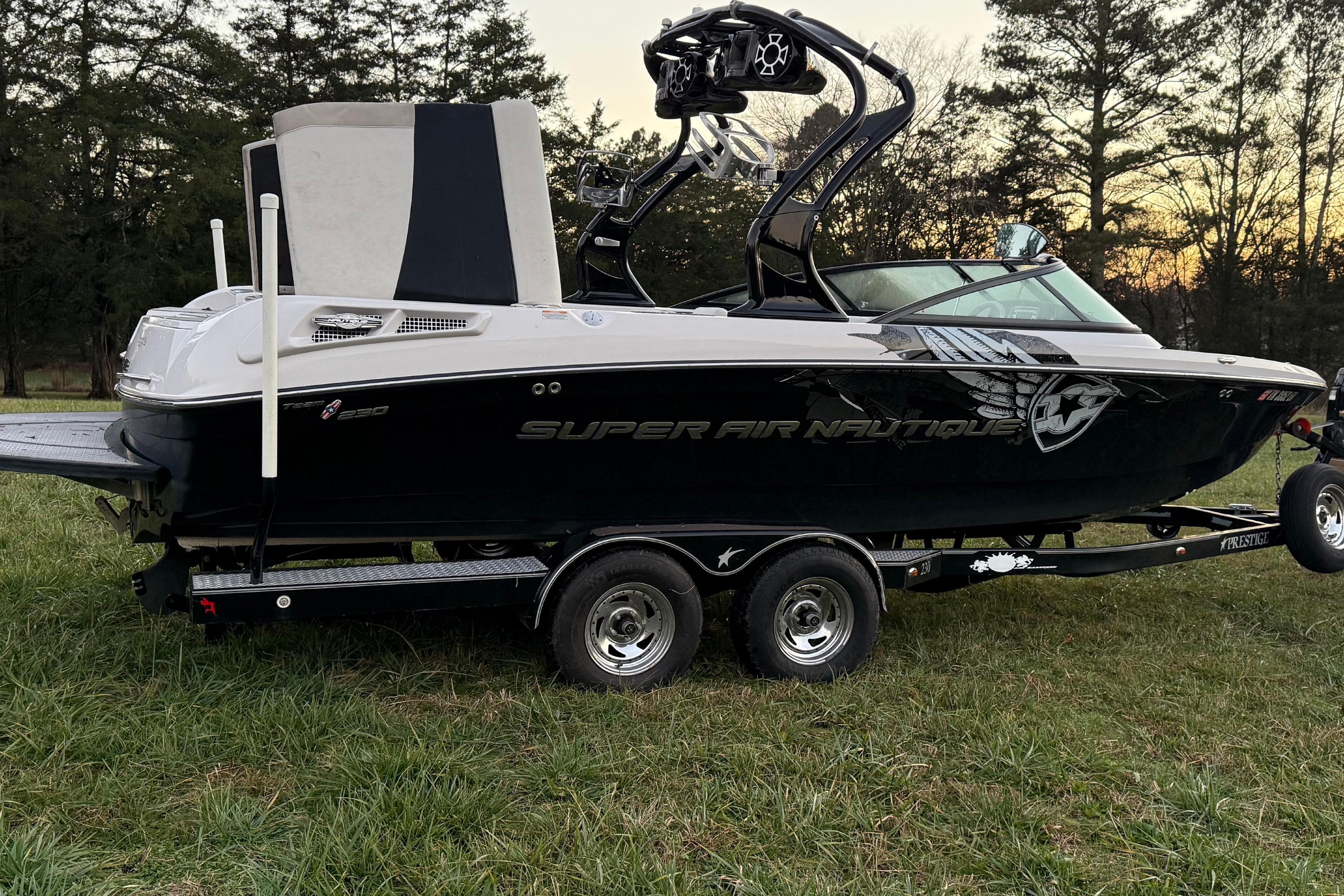 2010 Nautique Super Air Nautique 230 boat on trailer, parked on grass.