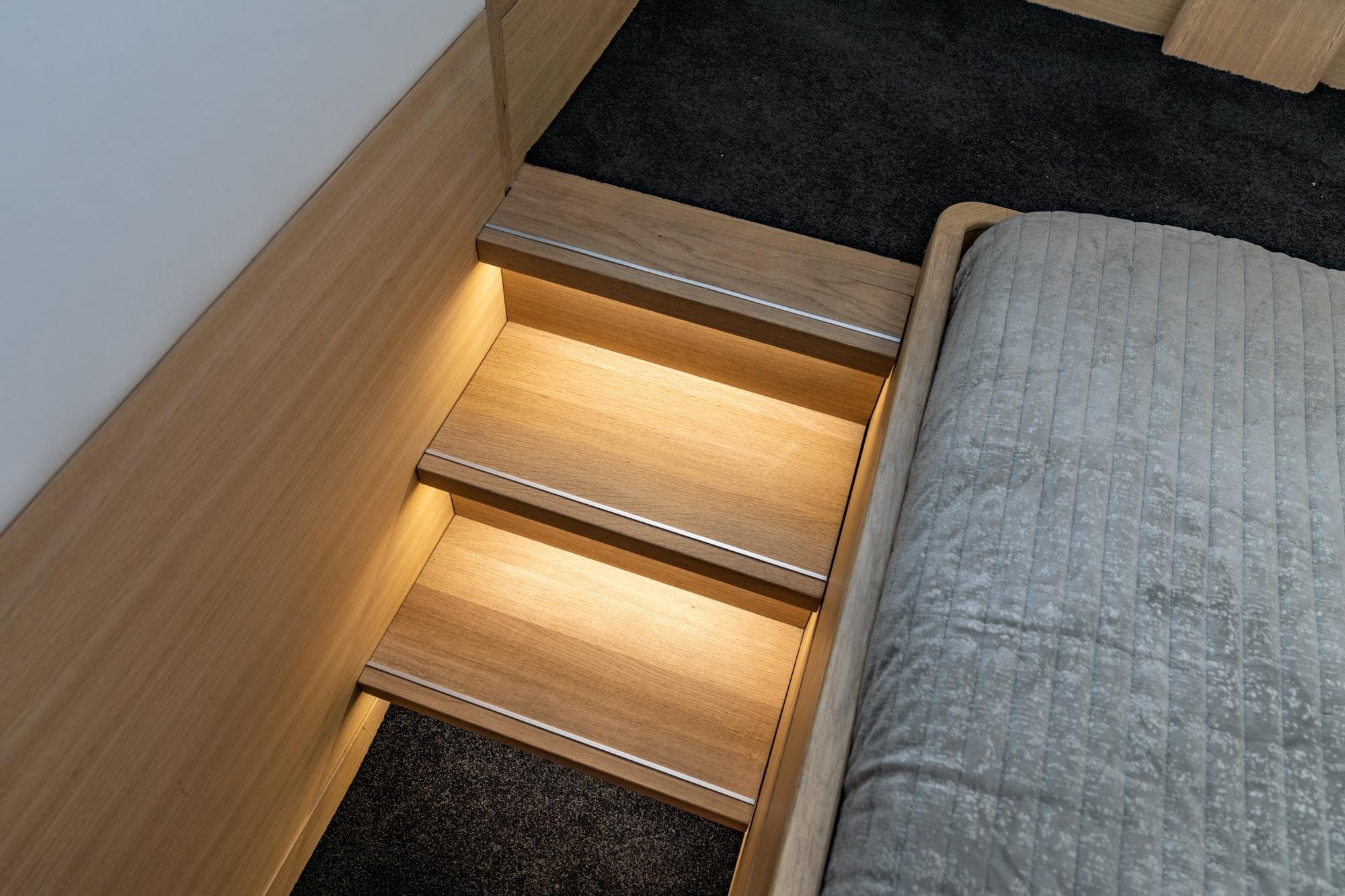 Wooden steps with ambient lighting beside a bed in a 2017 Steeler Panorama FF 53.
