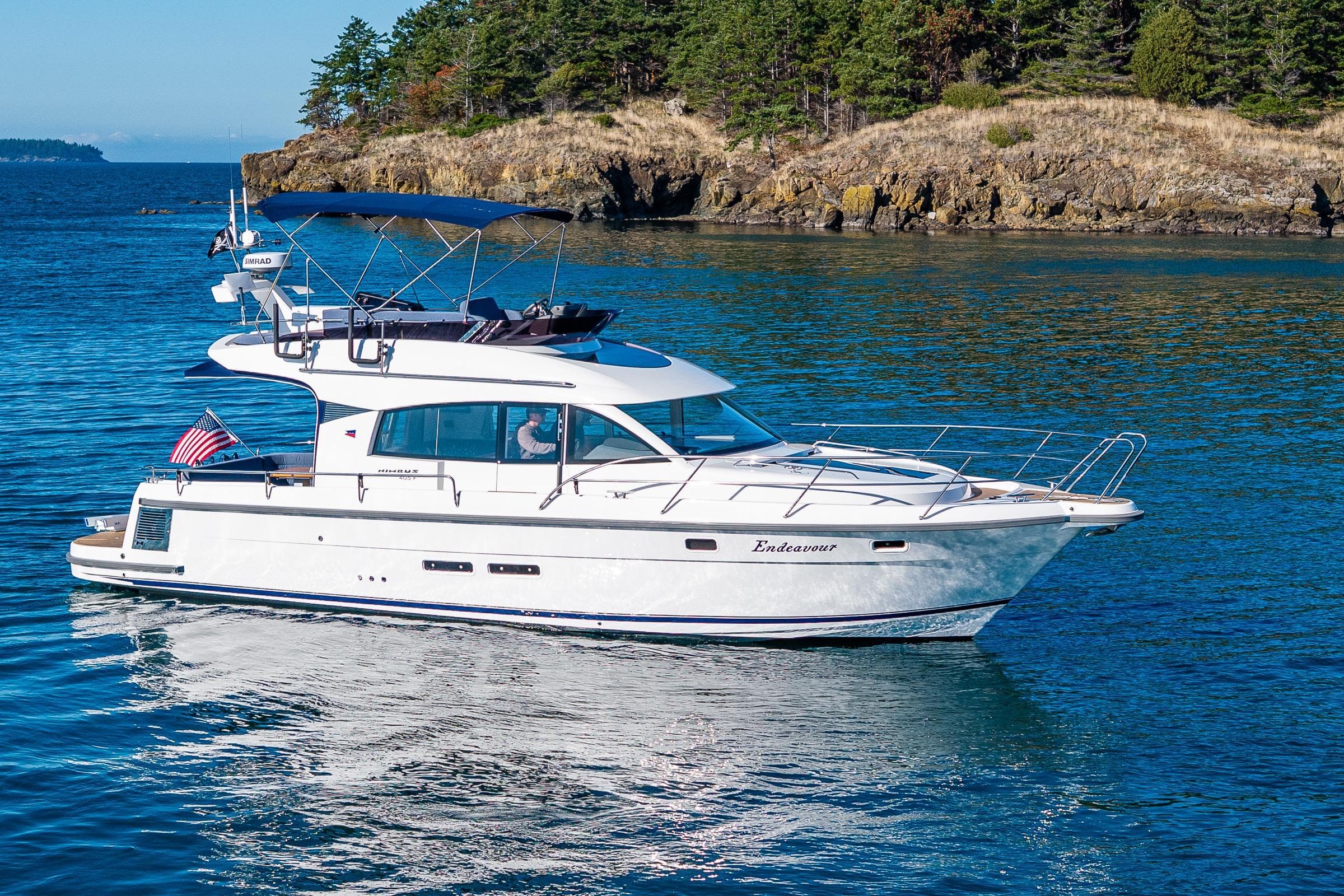 2023 Nimbus 405 Flybridge yacht cruising near rocky shoreline.