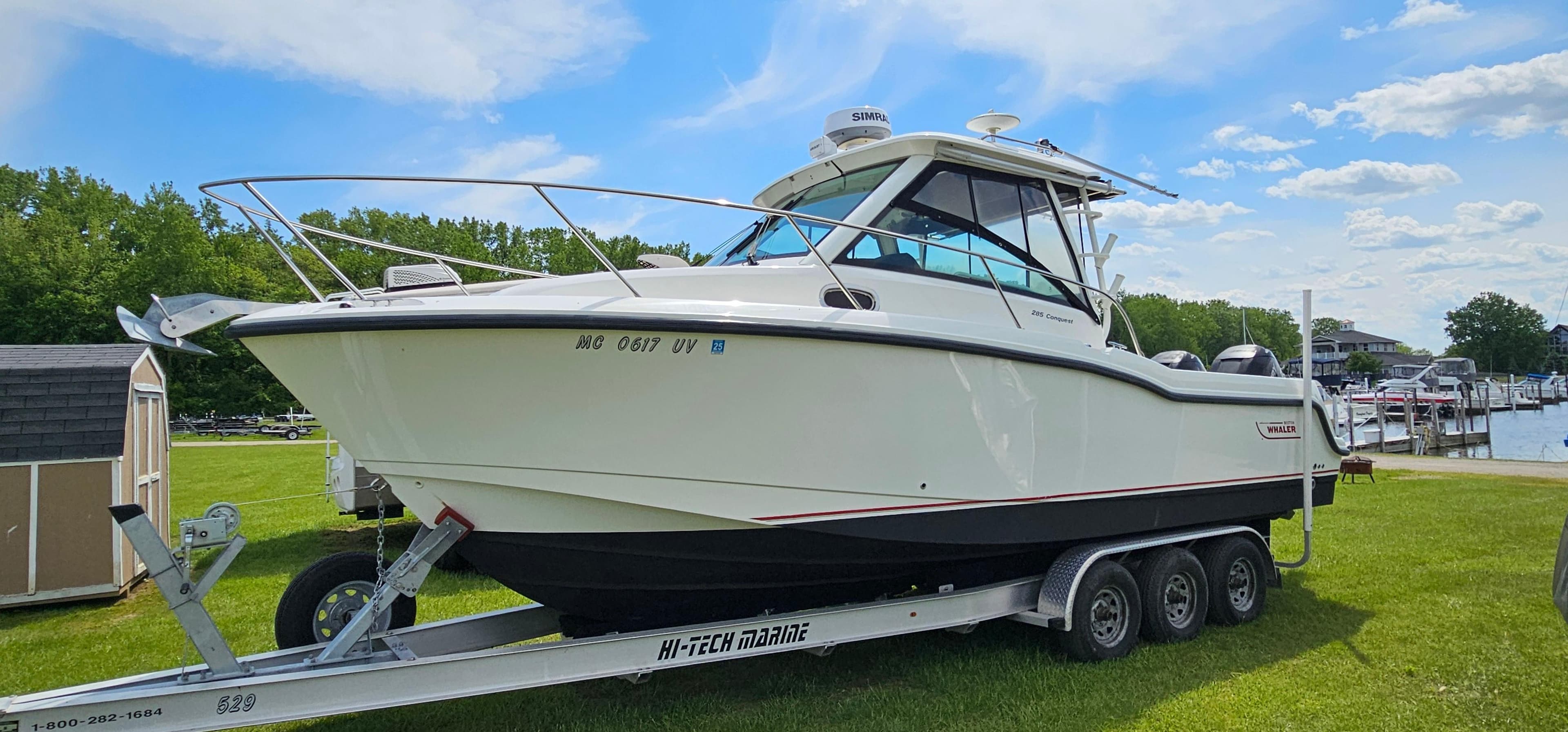 2016 Boston Whaler 285 Conquest boat on trailer, parked on grass under blue sky.