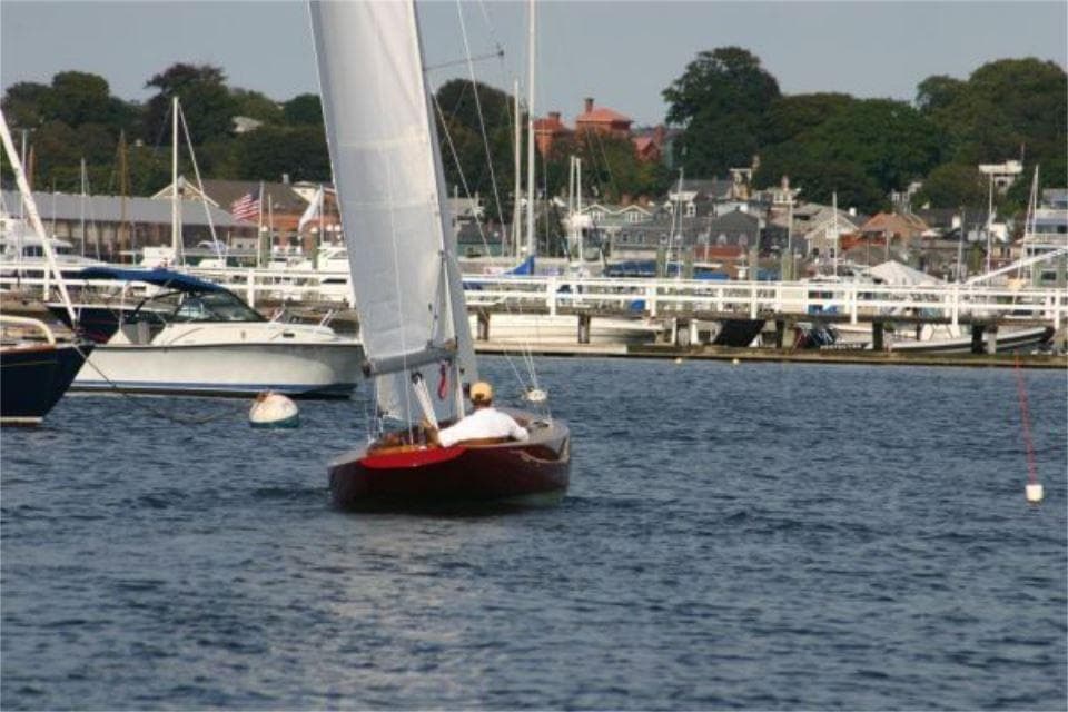 Sailboat Rustler 24 (2025) navigating a marina with other boats and waterfront buildings.