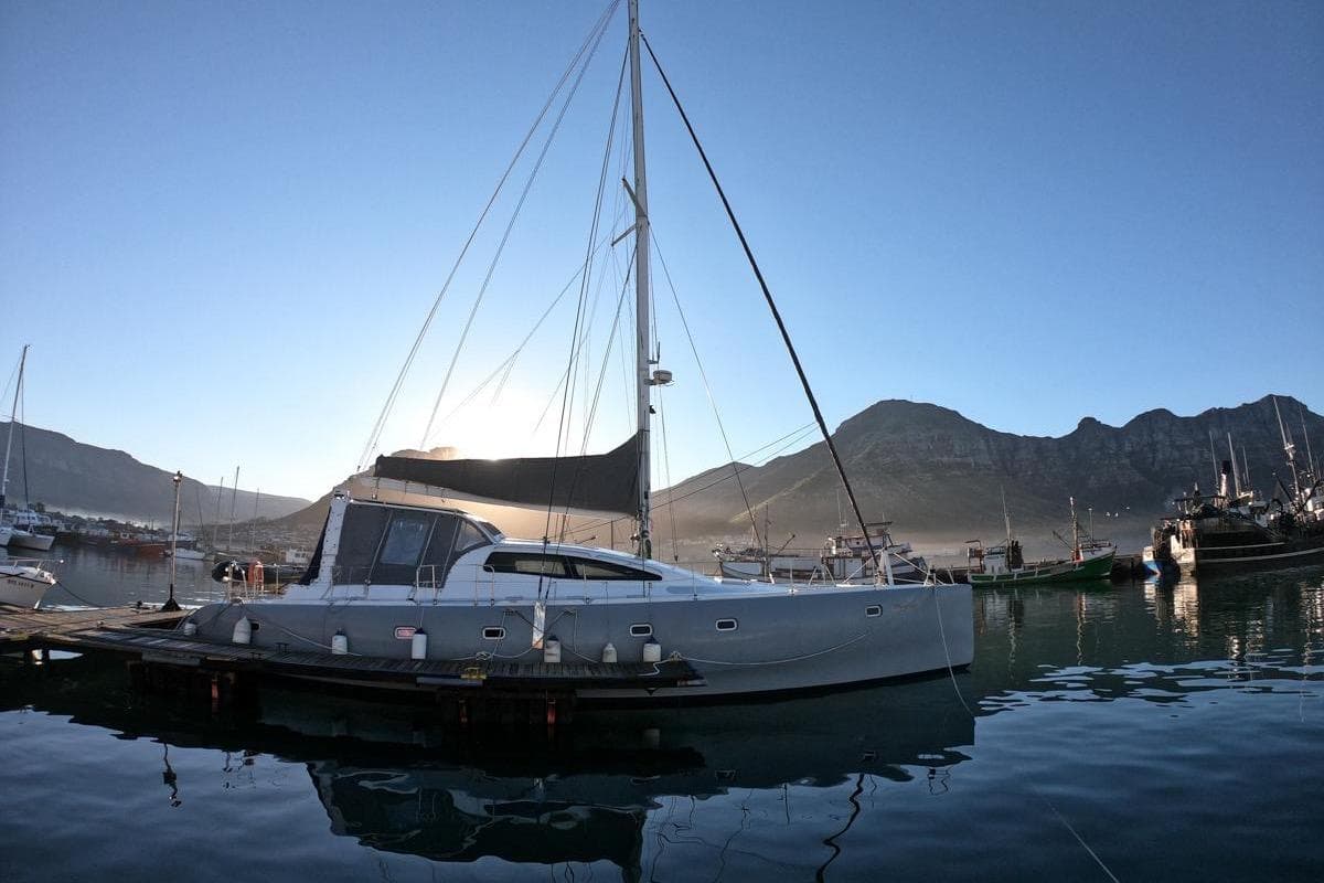 2006 Maxim Yachts 57 sailboat docked in a serene marina with mountain backdrop.