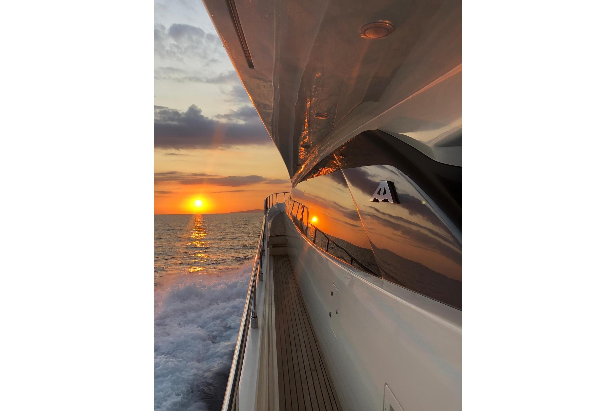 Astondoa 76 GLX yacht cruising at sunset, reflecting vibrant ocean and sky hues.