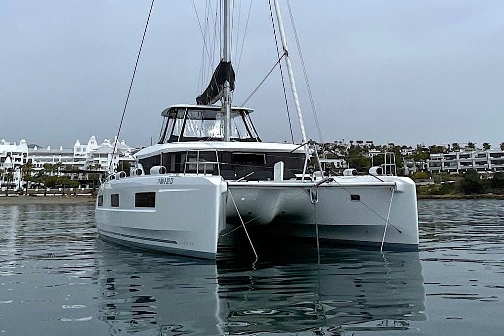 2023 Lagoon 46 catamaran anchored in calm waters near a coastal town.